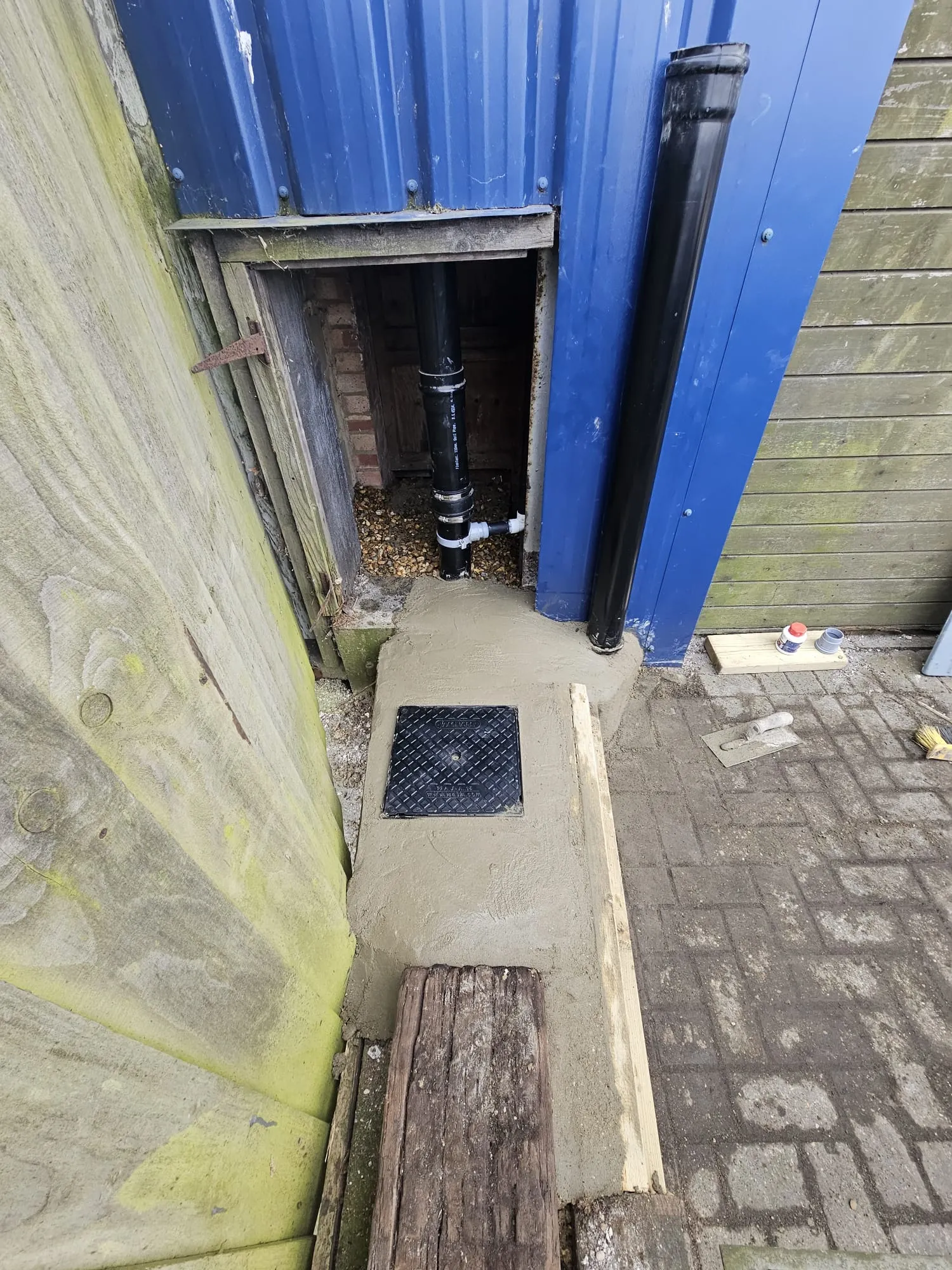 Newly installed drainage system with a black manhole cover in concrete and black drainage pipes, indicative of professional drainage installation or repair work.