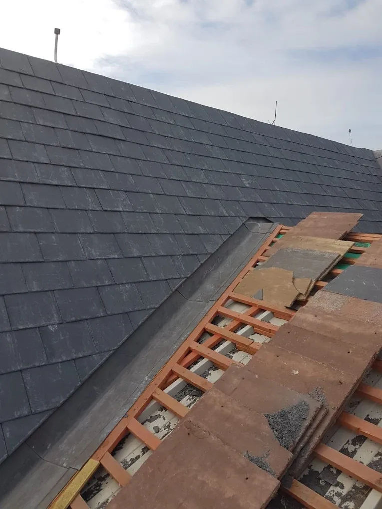 Pitched roof construction with slate tiles, lead valley gutter, exposed timber battens, and stacked clay tiles.