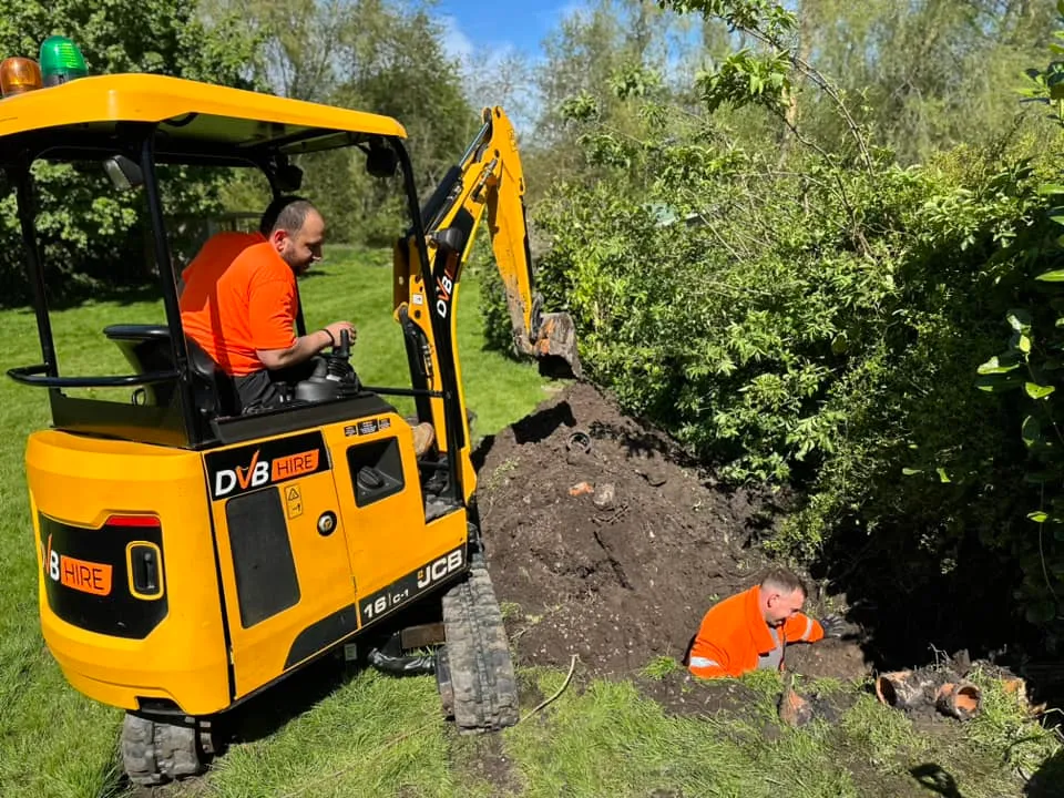 Drainage engineers from Drain 2 Flow Devon using a mini-excavator for drain repair or installation work in a garden setting in Devon.