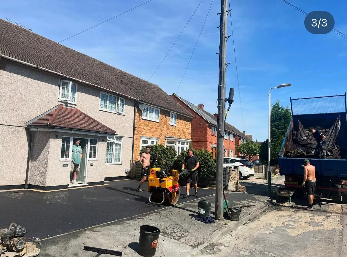 Top Pave Driveways LTD team installing a new tarmac driveway, with workers, a compactor, and a dump truck on a sunny day.