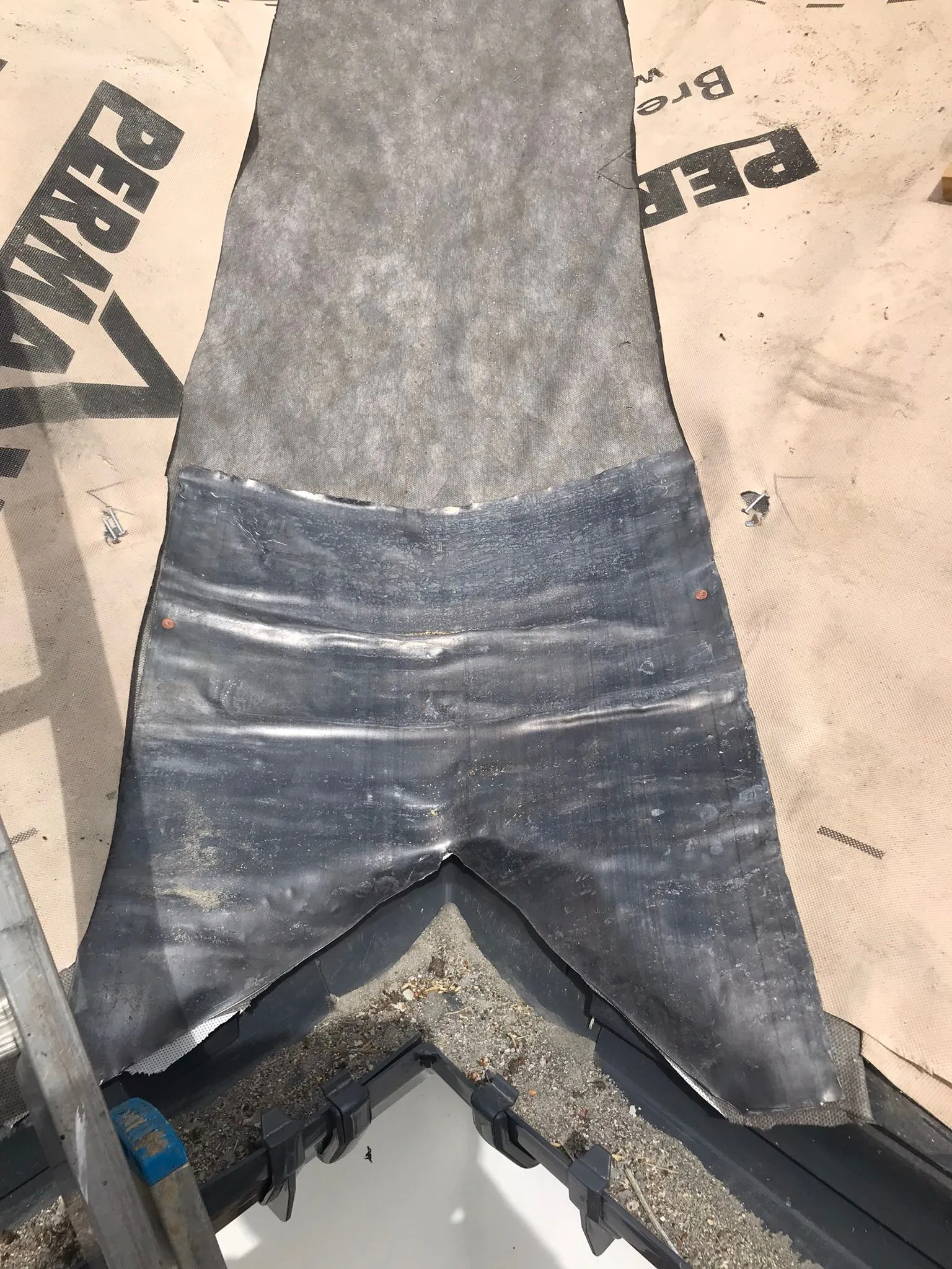 Close-up of lead flashing, roofing underlayment, and gutter components during a professional roof installation or repair.