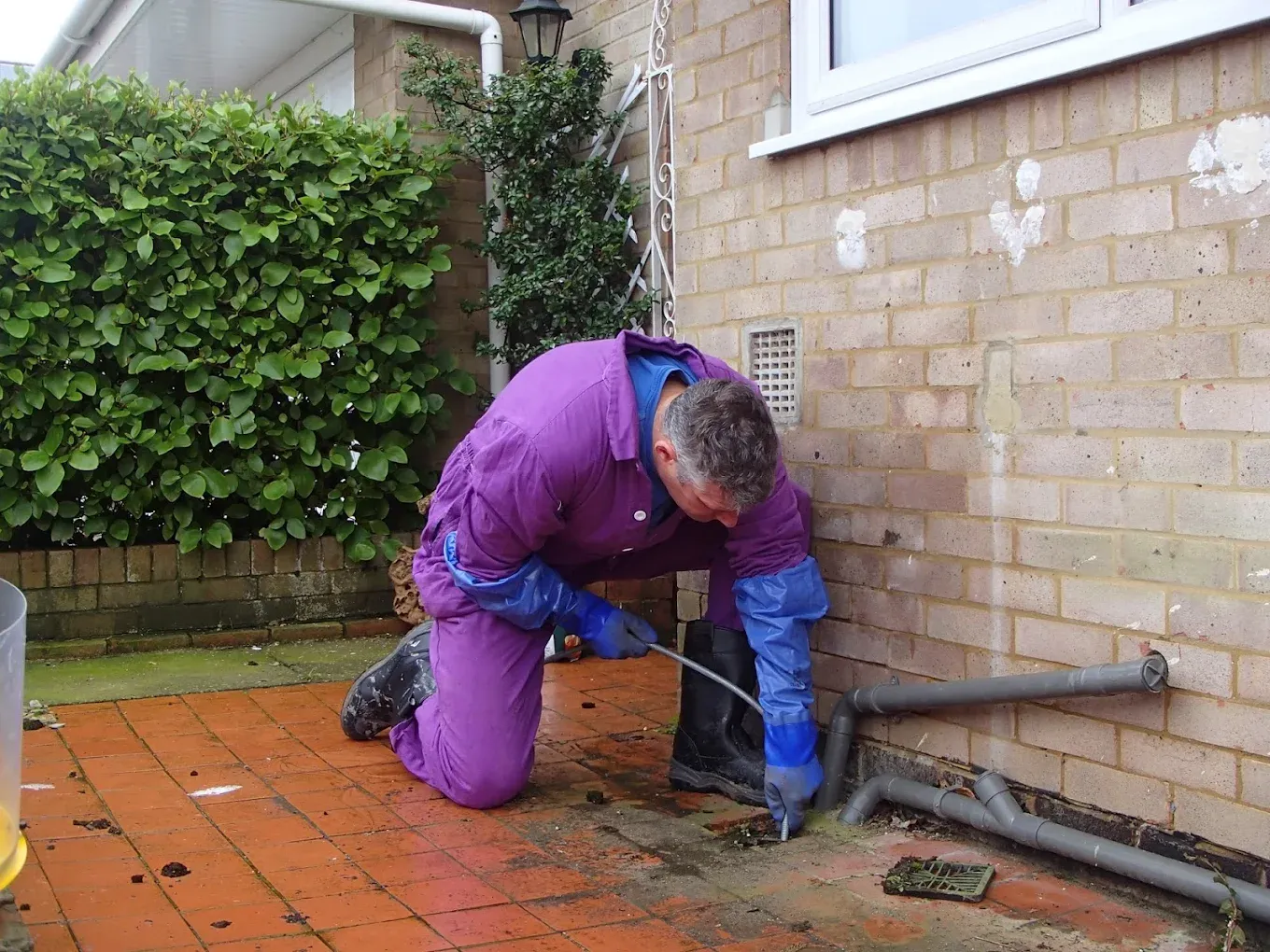 Drainage engineer clearing or repairing an exterior drain at a residential property.