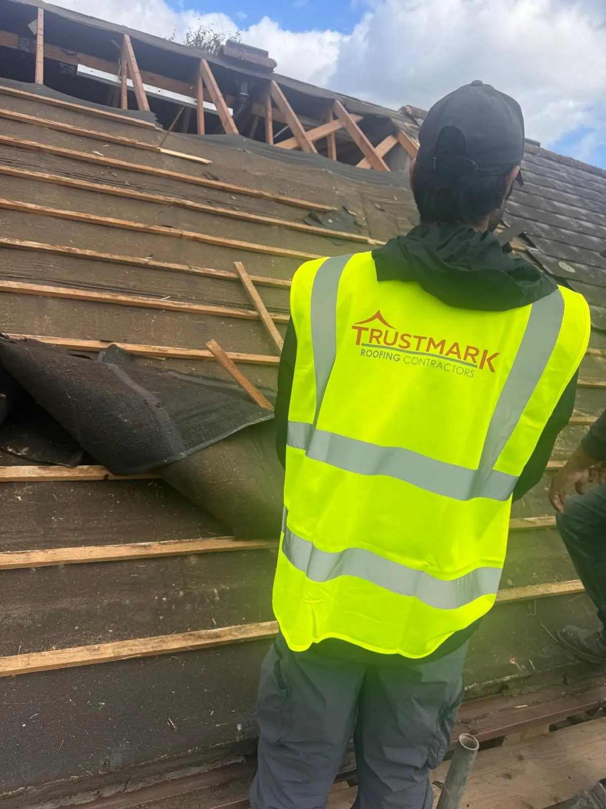 Trustmark Roofing roofer in high-vis vest on a partially stripped pitched roof showing battens and underlay.