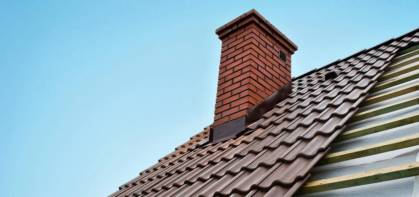 Close-up of new roof tiles being installed around a red brick chimney stack.
