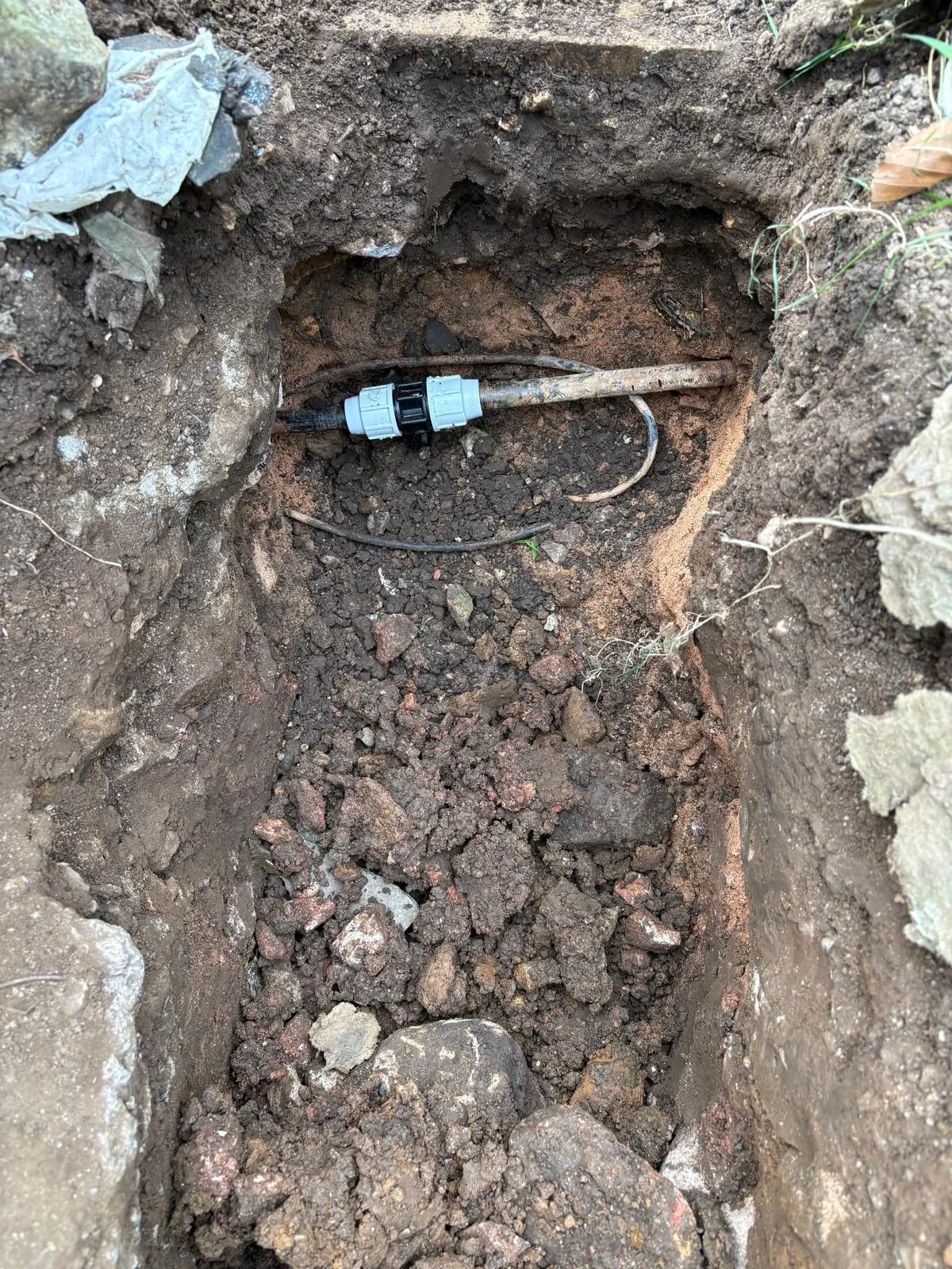 An underground pipe being repaired or installed in an excavated trench with a visible connection fitting.
