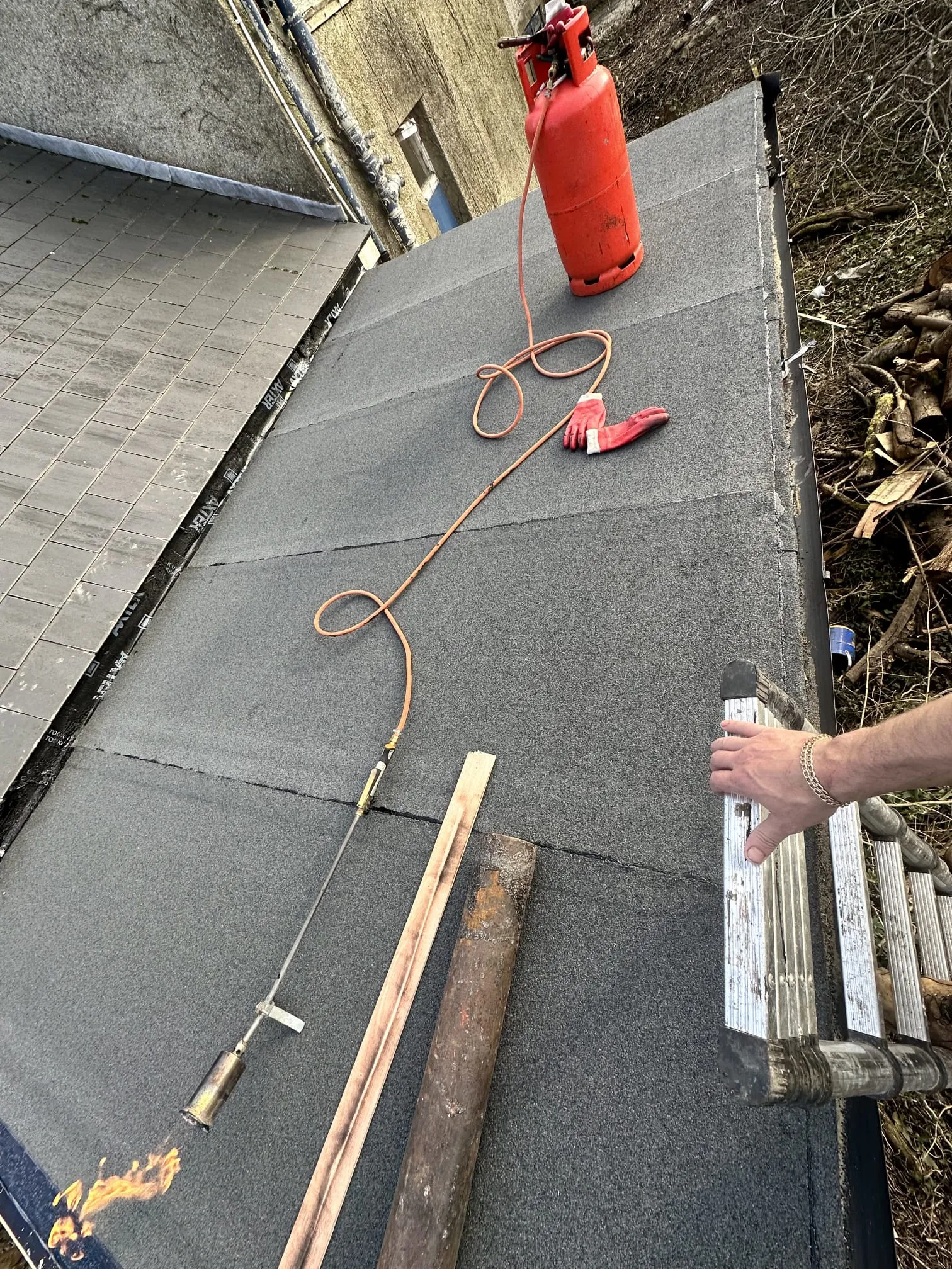 An image showing the installation of a new felt flat roof using the torch-on method, with a roofer's equipment on the roof.