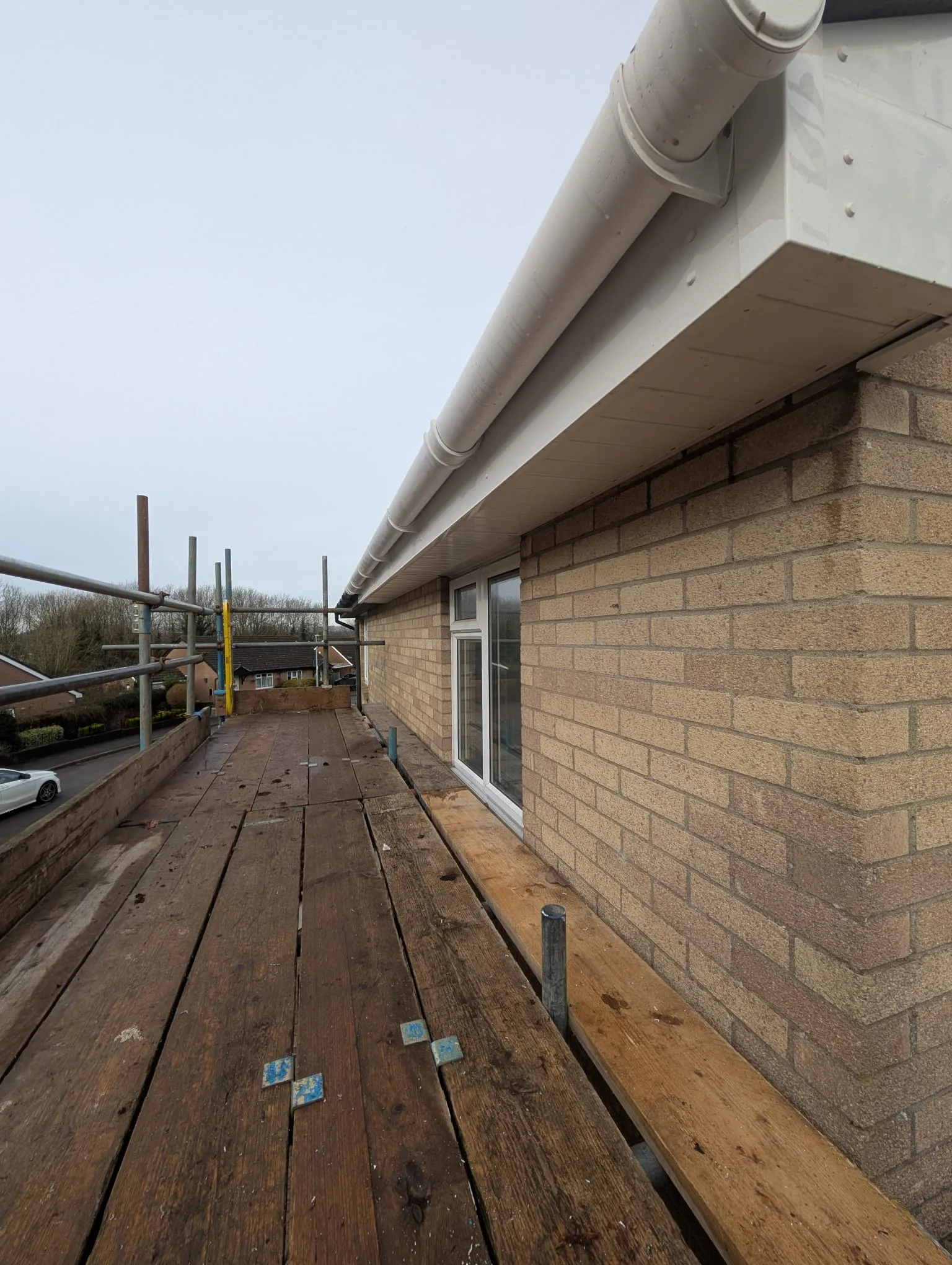 New white uPVC fascias, soffits, and guttering installed on a brick house, seen from the perspective of scaffolding.