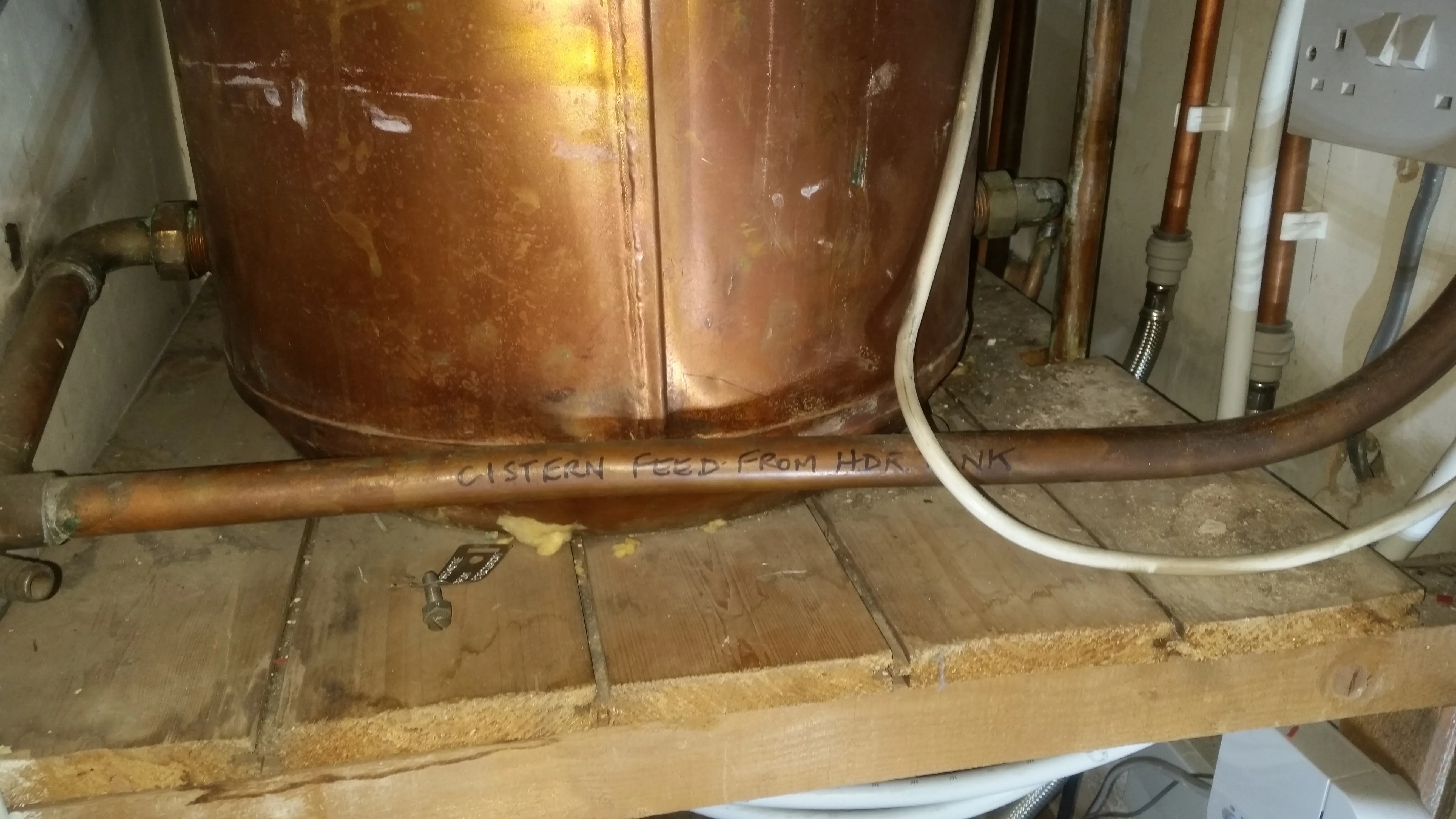 A copper hot water tank with pipes, including one labelled 'CISTERN FEED', in a domestic setting.
