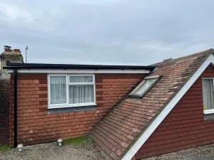 A new flat roof with black uPVC fascias and gutters next to a tiled pitched roof with a Velux window.