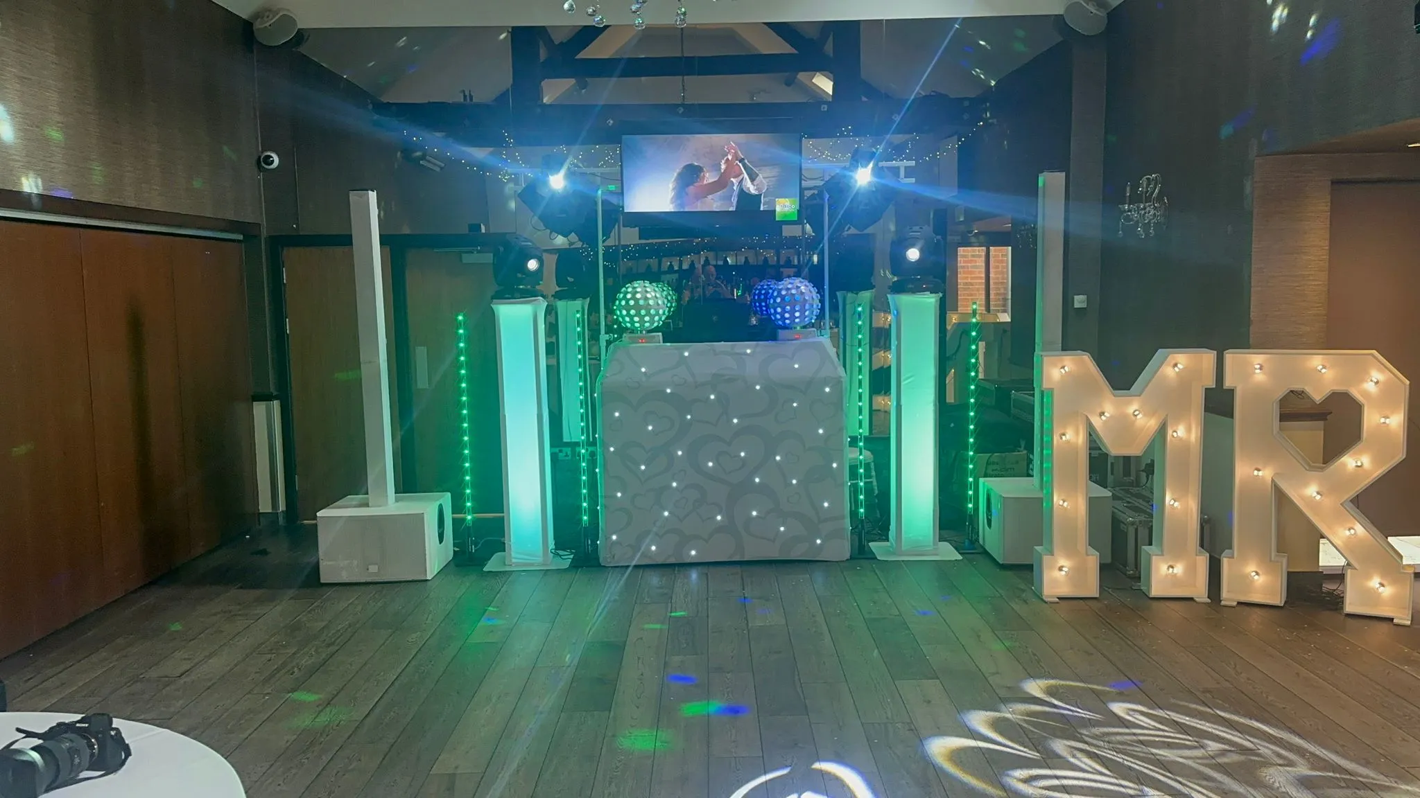 Award-winning wedding DJ setup with green lighting, big screens, and 'MR' light-up letters for an unforgettable reception.