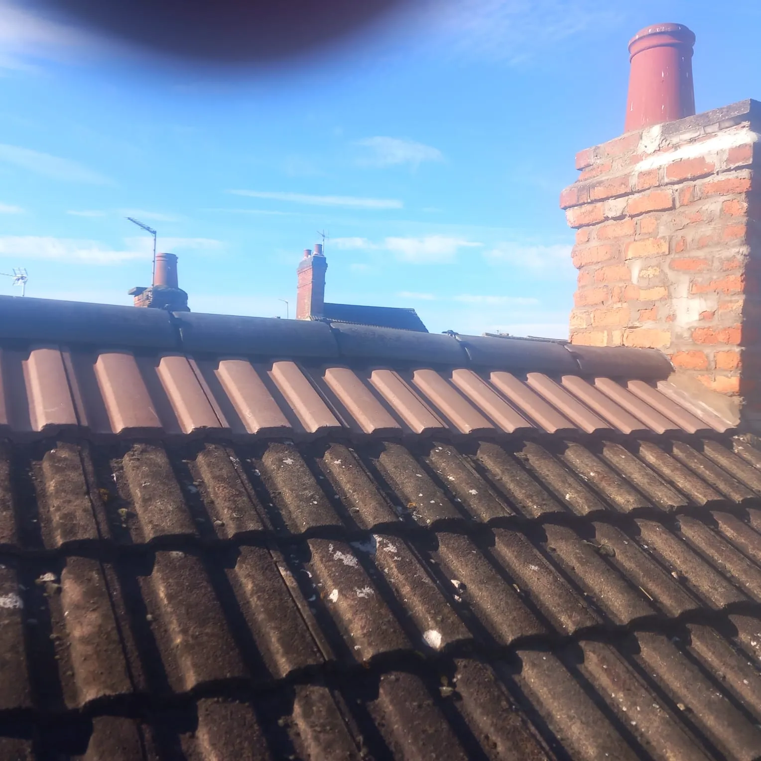 Tiled roof in Leicestershire showing old, mossy tiles alongside new, clean brown tiles, with a brick chimney and blue sky. Represents roof repair, re-roofing, chimney work, or moss removal services by 5 Star Roofing Leicester.
