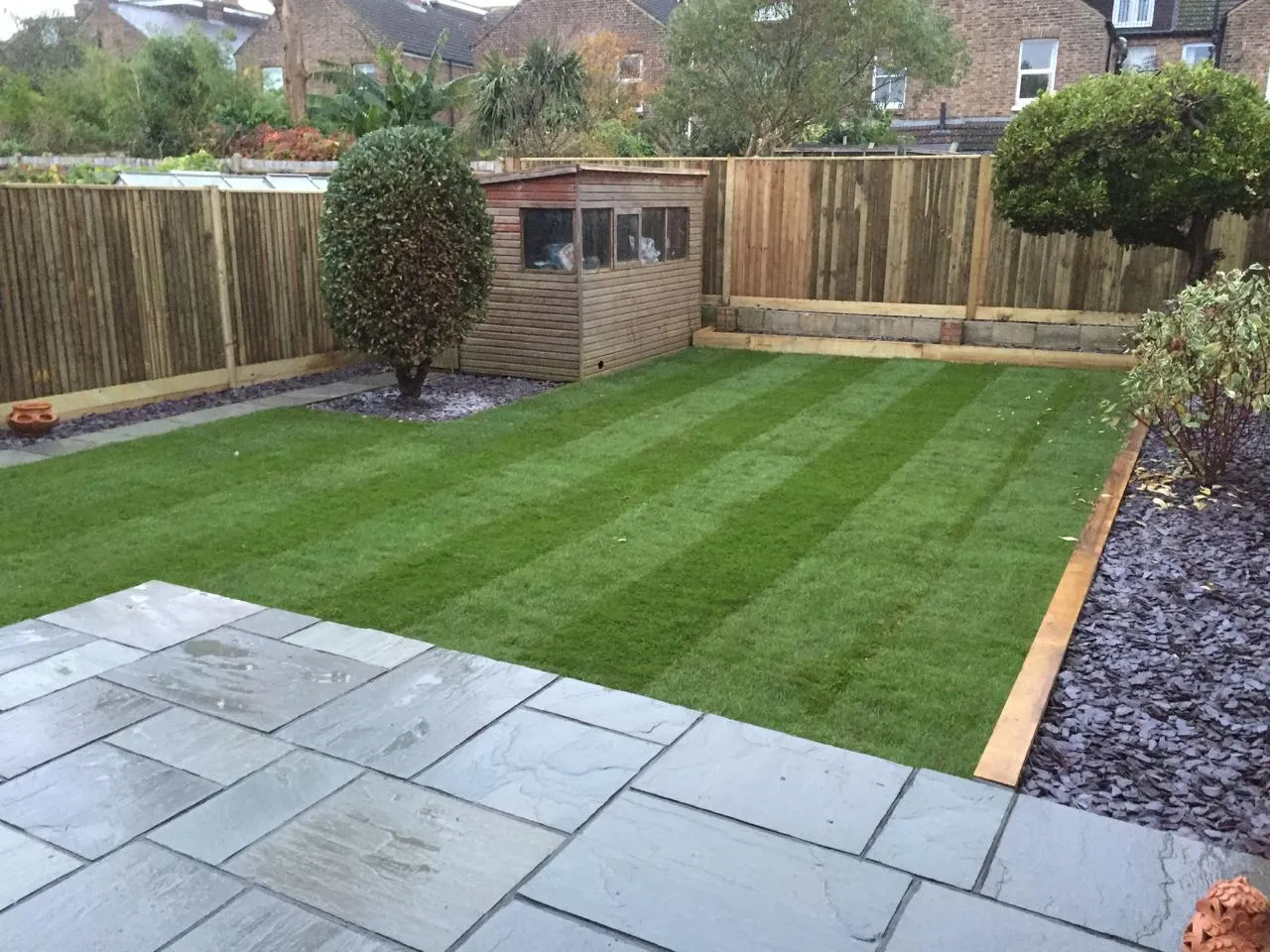 Completed garden makeover with patio, striped lawn, new fencing, and slate chippings.