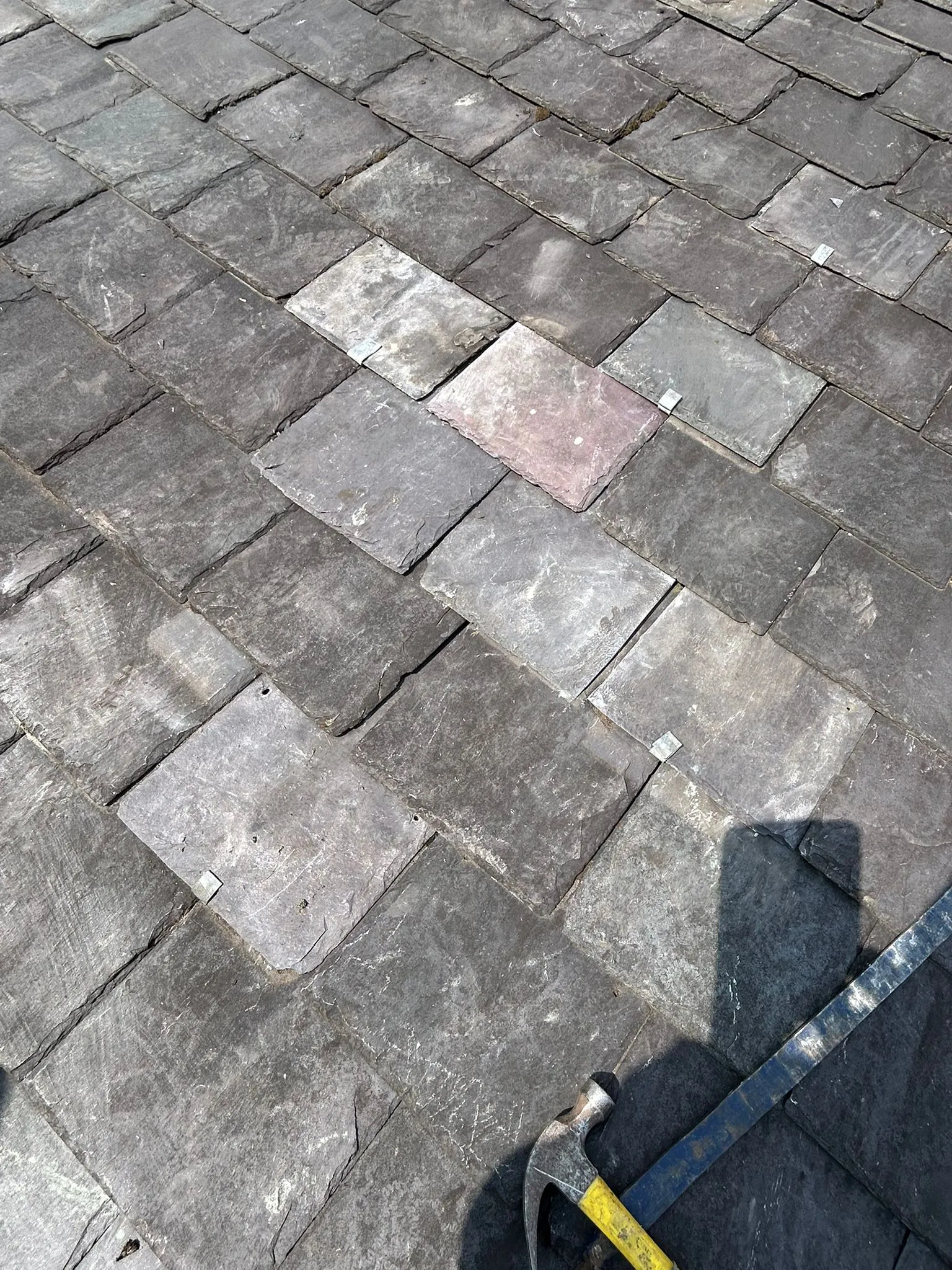 Close-up of a slate roof with new and old slates, showing metal repair clips and roofing tools.