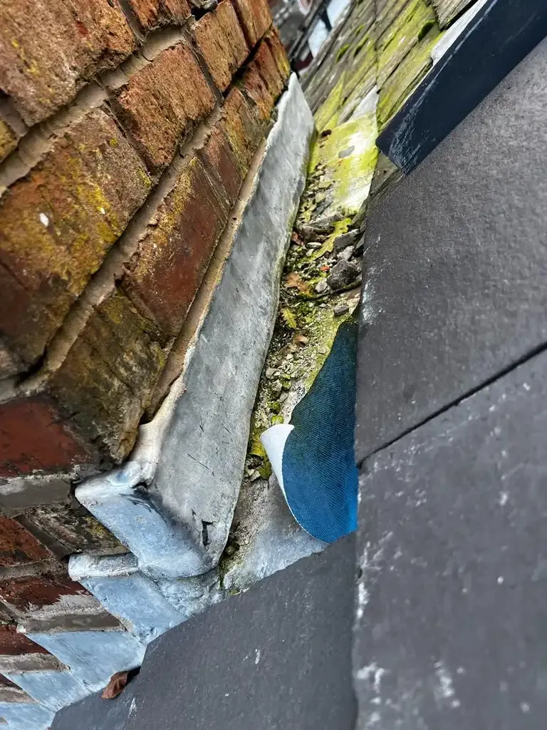Close-up of a roof valley with debris, lead flashing, and roof tiles, indicating a potential leak issue.