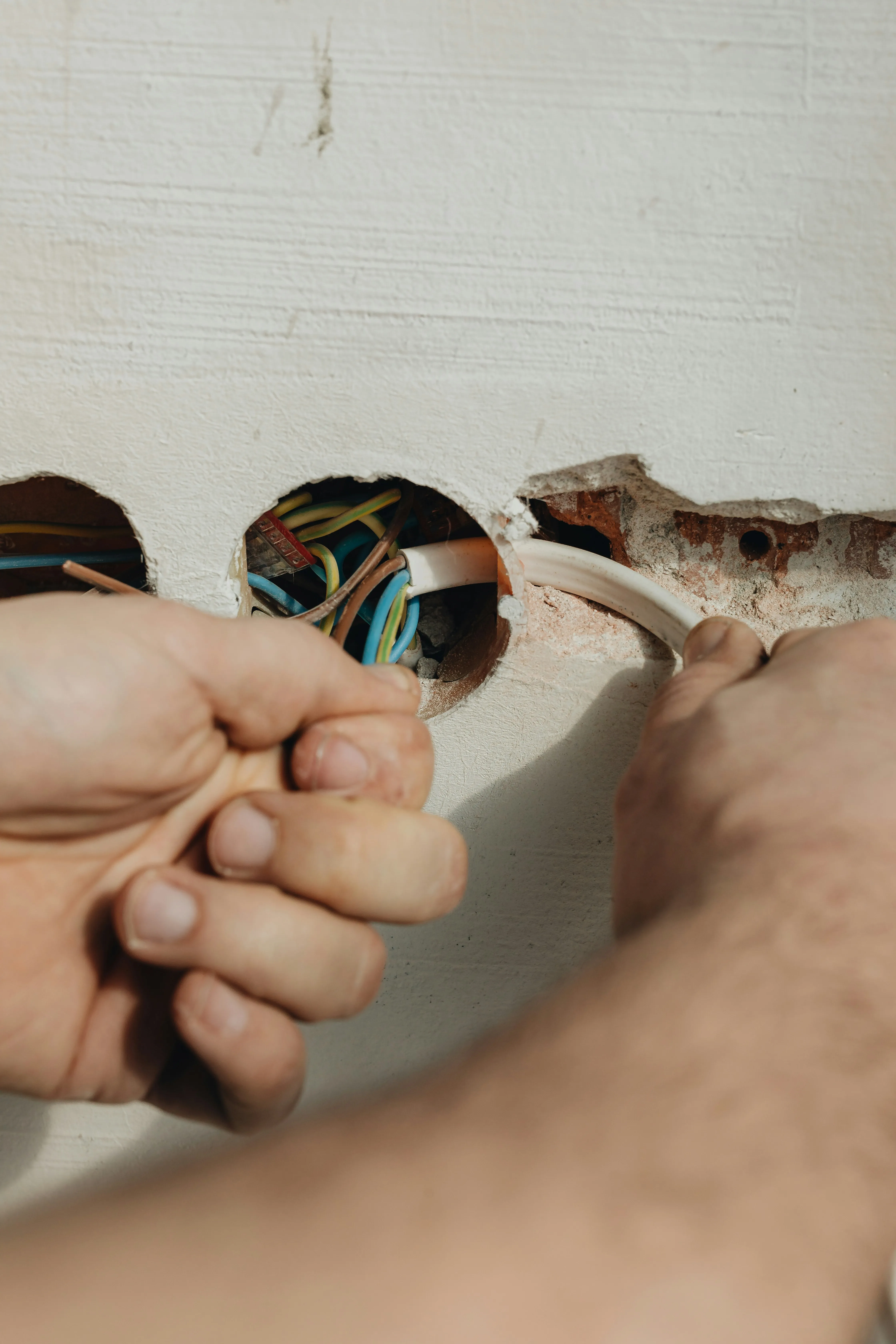 Close-up of an electrician's hands installing electrical wiring for a new socket or switch in a wall.