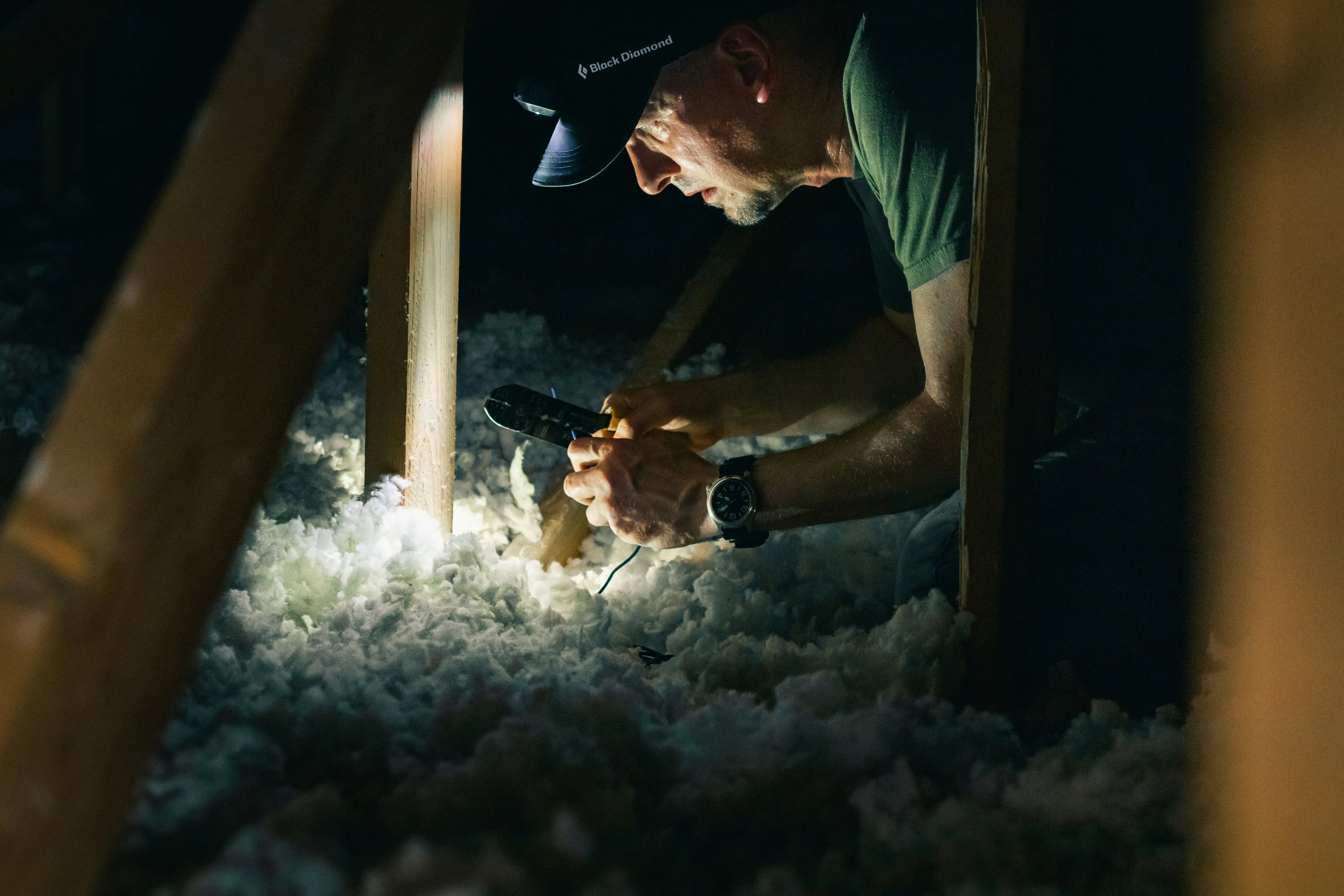 A Moorlander Pest Control technician with a headlamp and tools, inspecting a dark loft space with insulation for pest activity or damage.