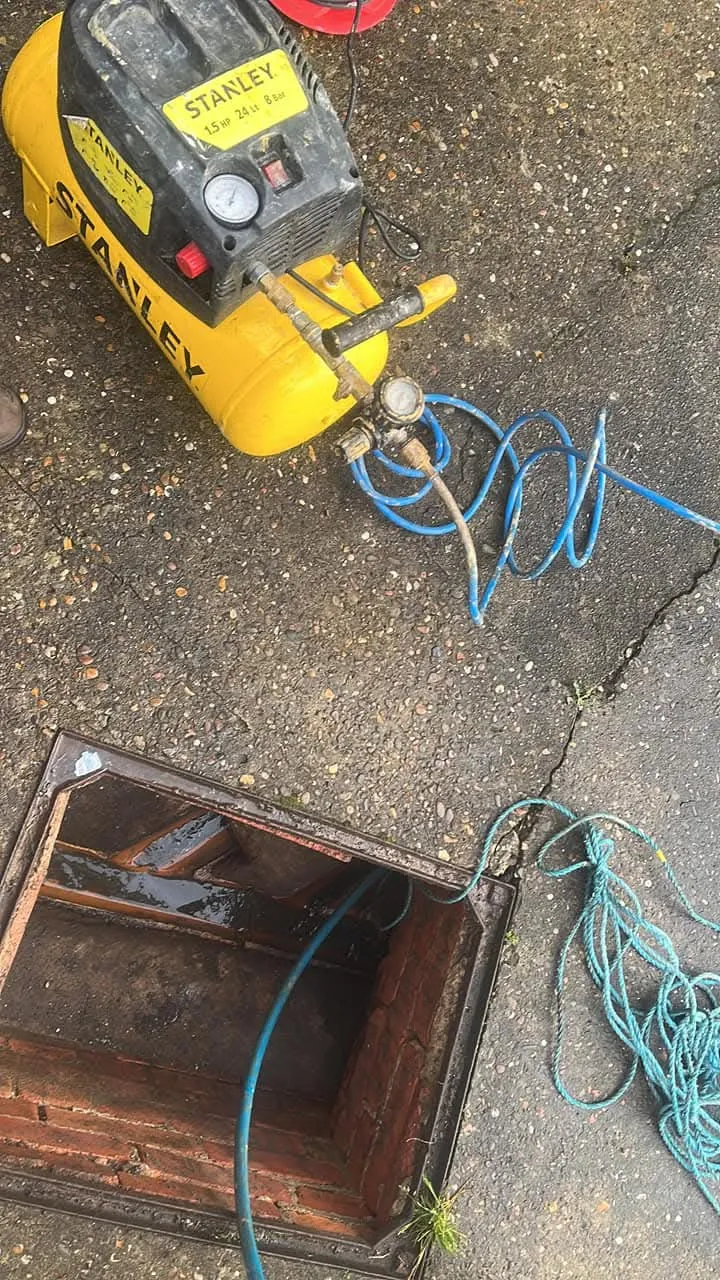 Air compressor and hose at an open drain or manhole