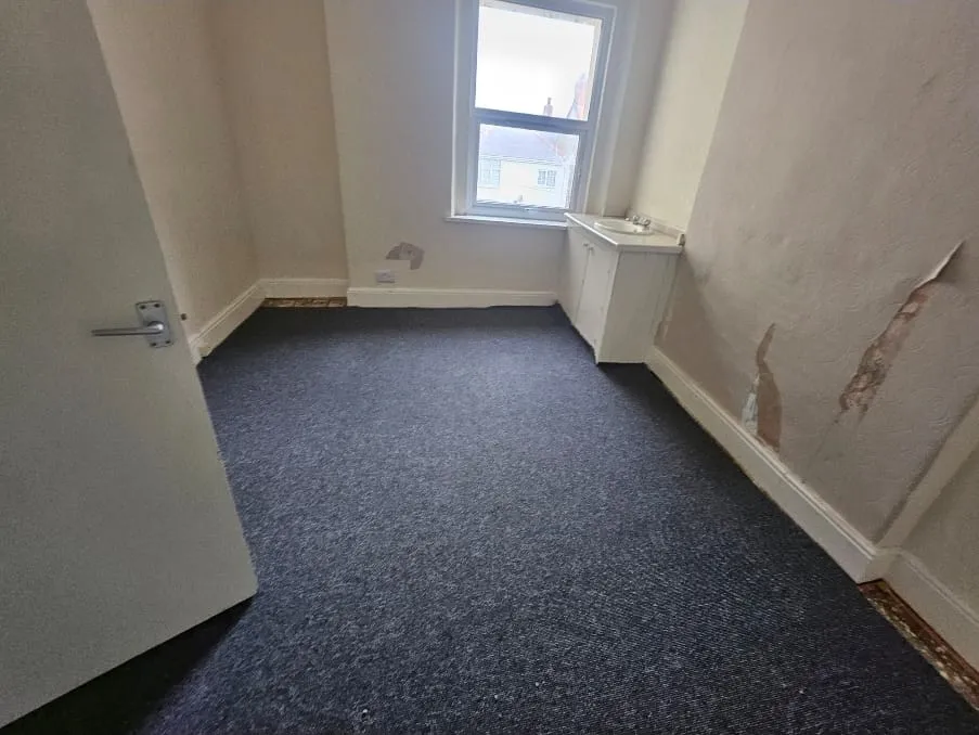 An empty room with blue carpet and damaged walls, ready for an end-of-tenancy or house clearance service.