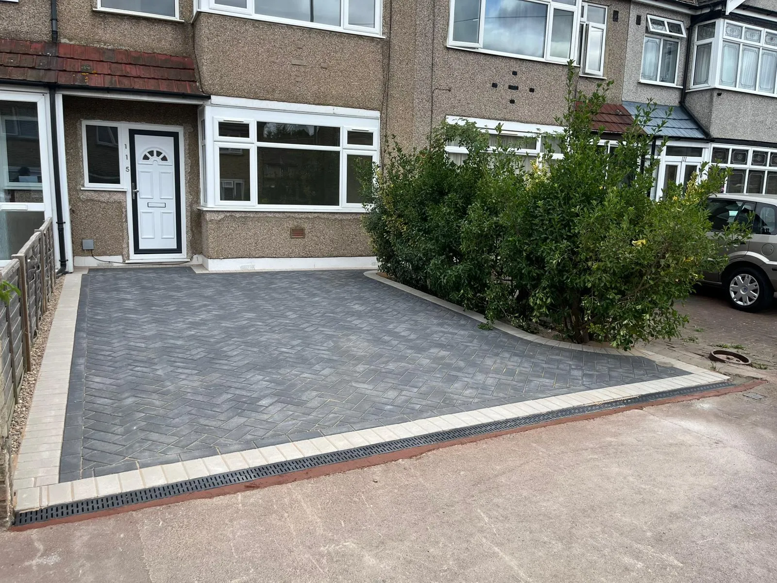 New block paving driveway installation with a herringbone pattern, light-coloured border, and integrated linear drainage channel leading to a modern white front door of a Romford home.