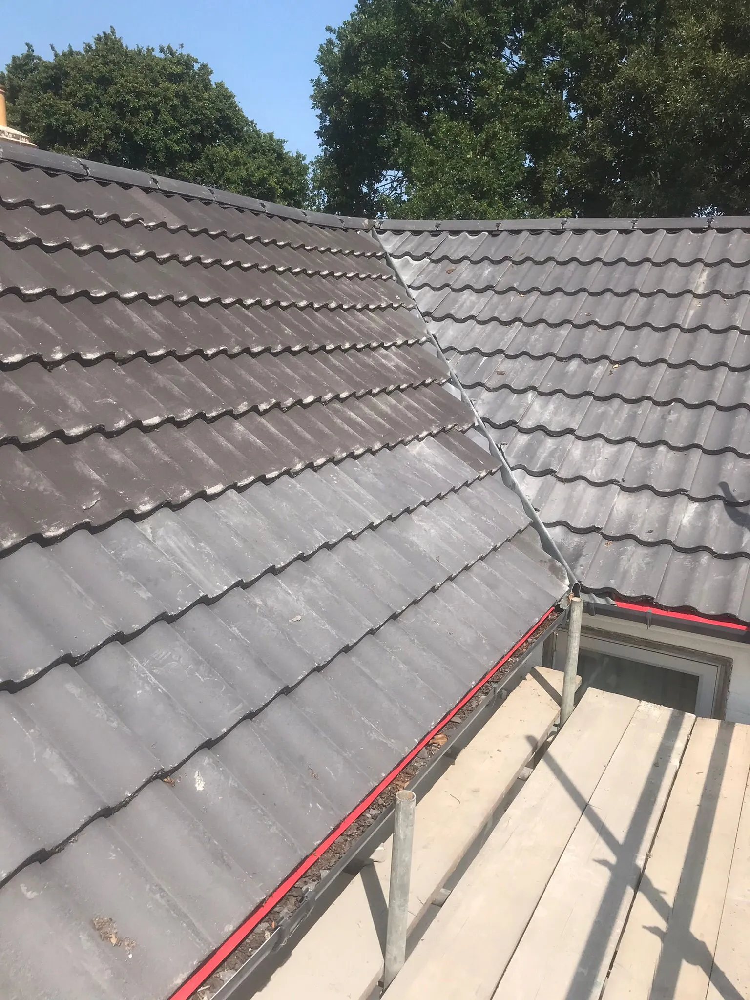 Tiled roof showing a cleaned section and an uncleaned section, with scaffolding in place for roof maintenance.