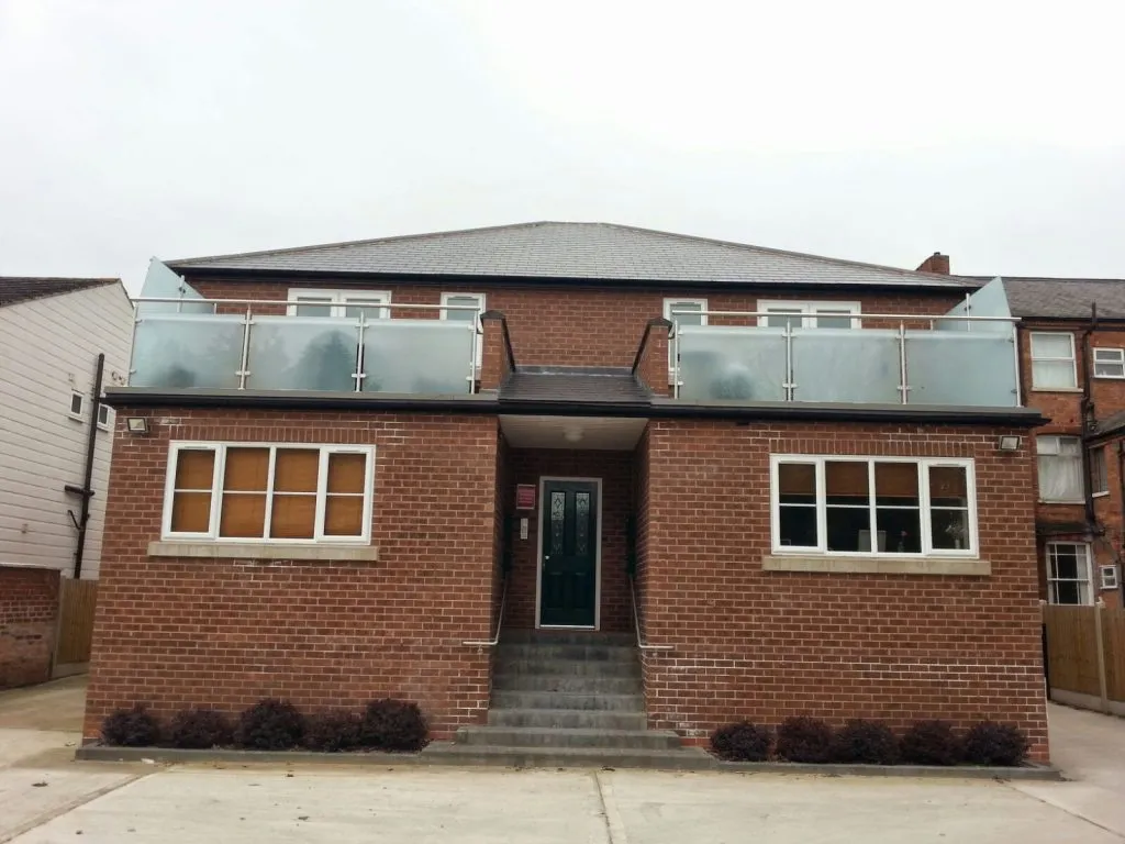 Modern brick building with a new grey pitched roof and two flat roof balconies featuring glass railings.