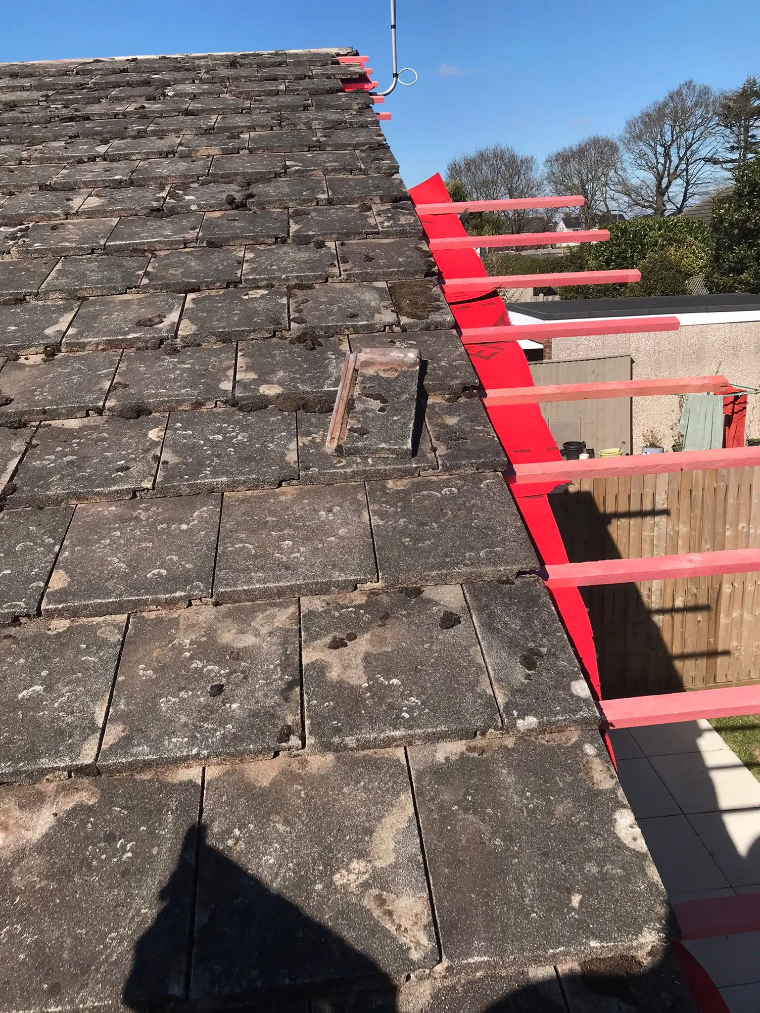 An image of an old, mossy tiled roof next to a section with new red roofing felt and horizontal wooden battens, indicating roof repair or replacement work in progress.