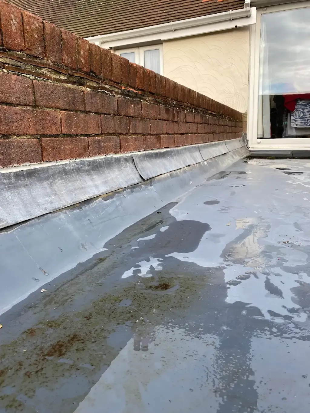 Damaged lead flashing and standing water on a flat roof.