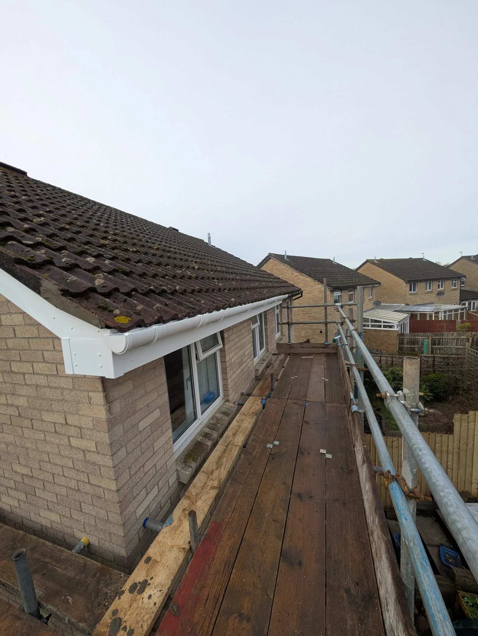 Scaffolding next to a house with newly installed white uPVC fascias and guttering on a tiled roof.