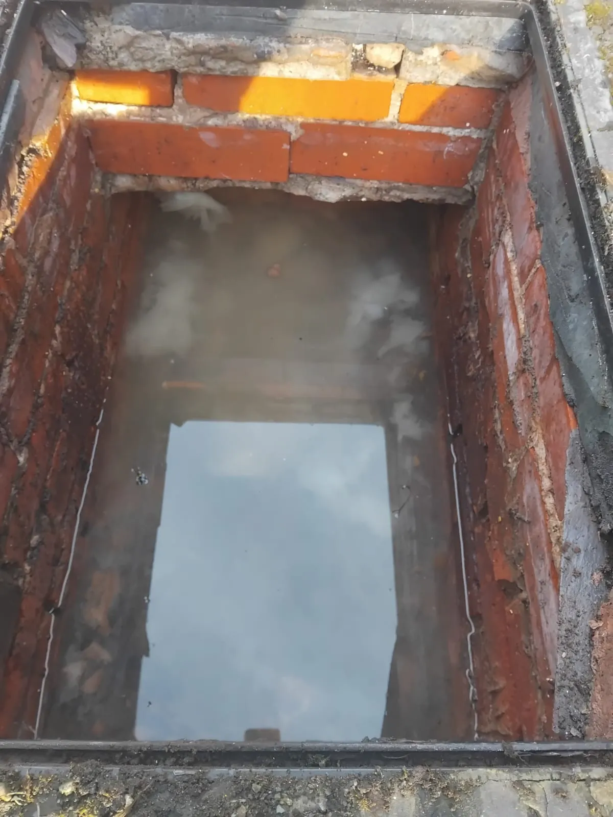 A blocked or overflowing drain inspection chamber filled with standing murky water, showing a drainage problem.