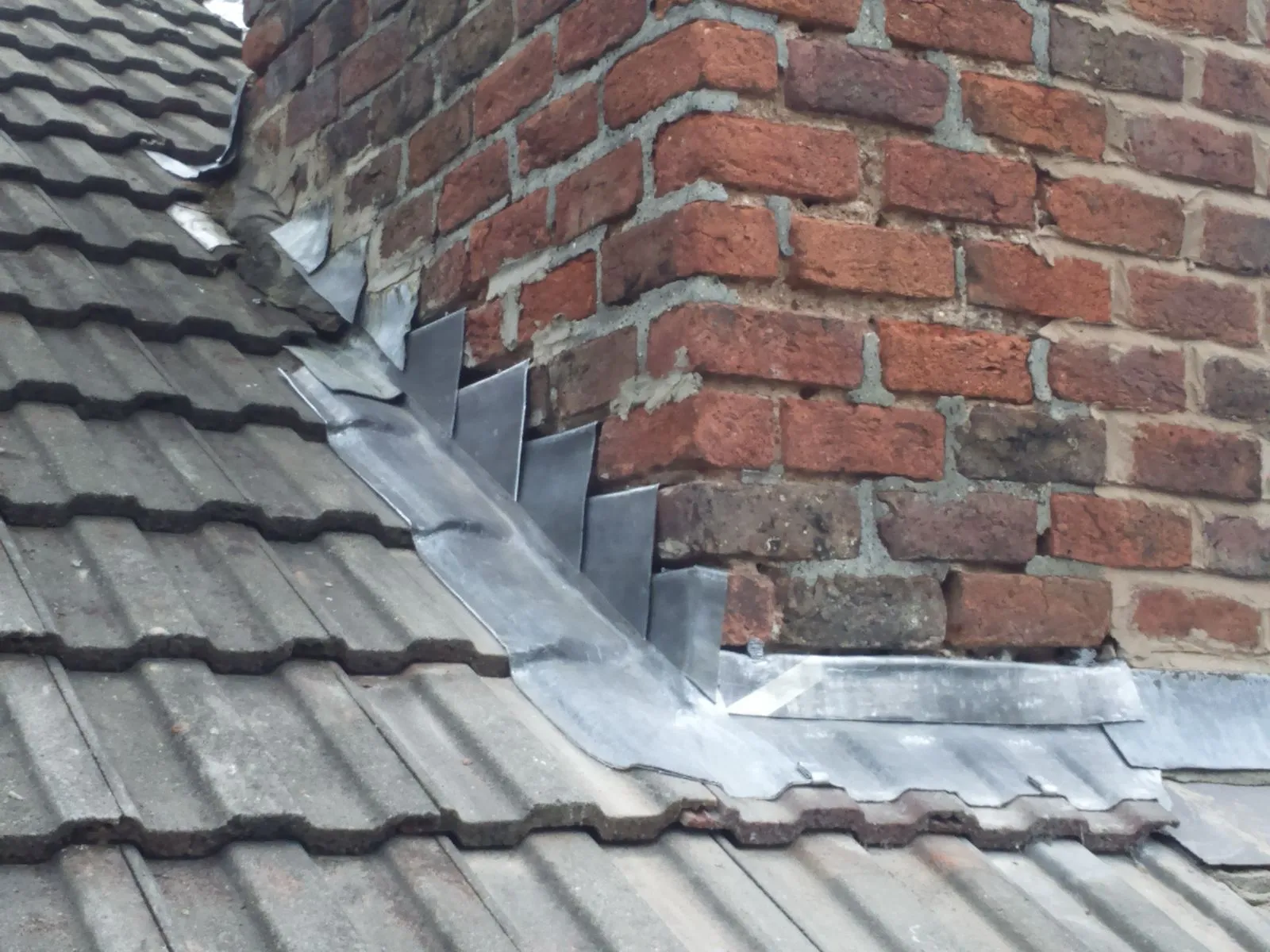 Lead flashing protecting a chimney stack on a tiled roof.