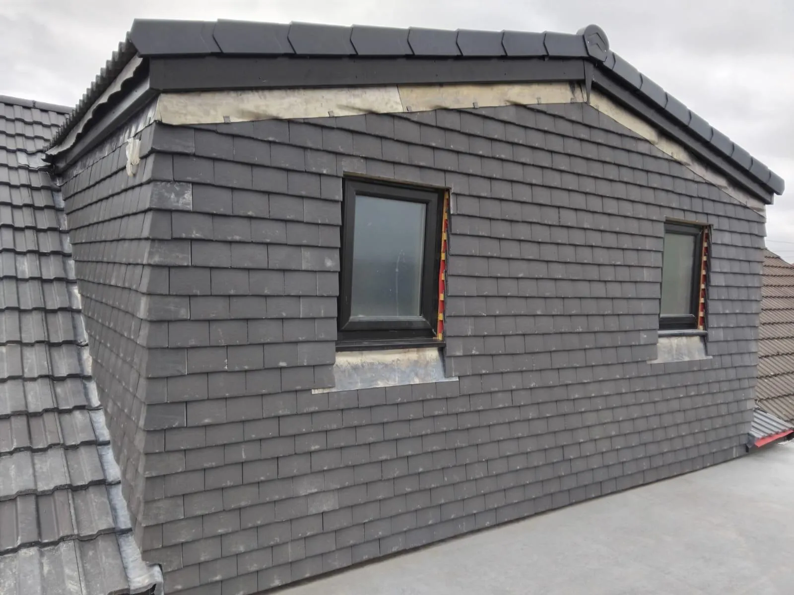 Close-up of a modern dormer roof with new dark grey slate tile cladding and two windows.
