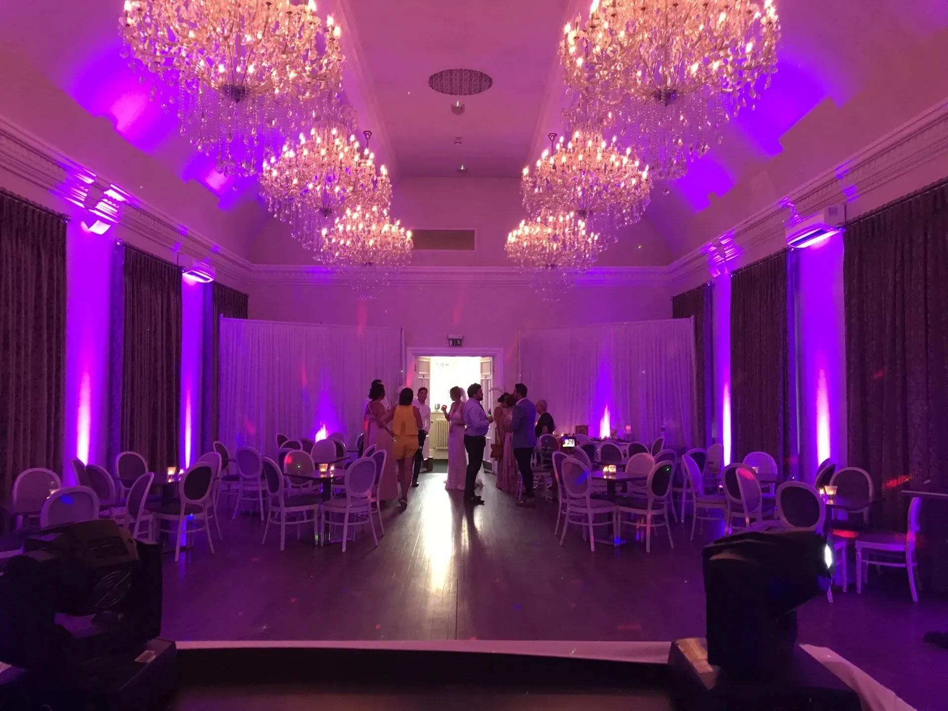 Event venue decorated with purple uplighting, chandeliers, and guests