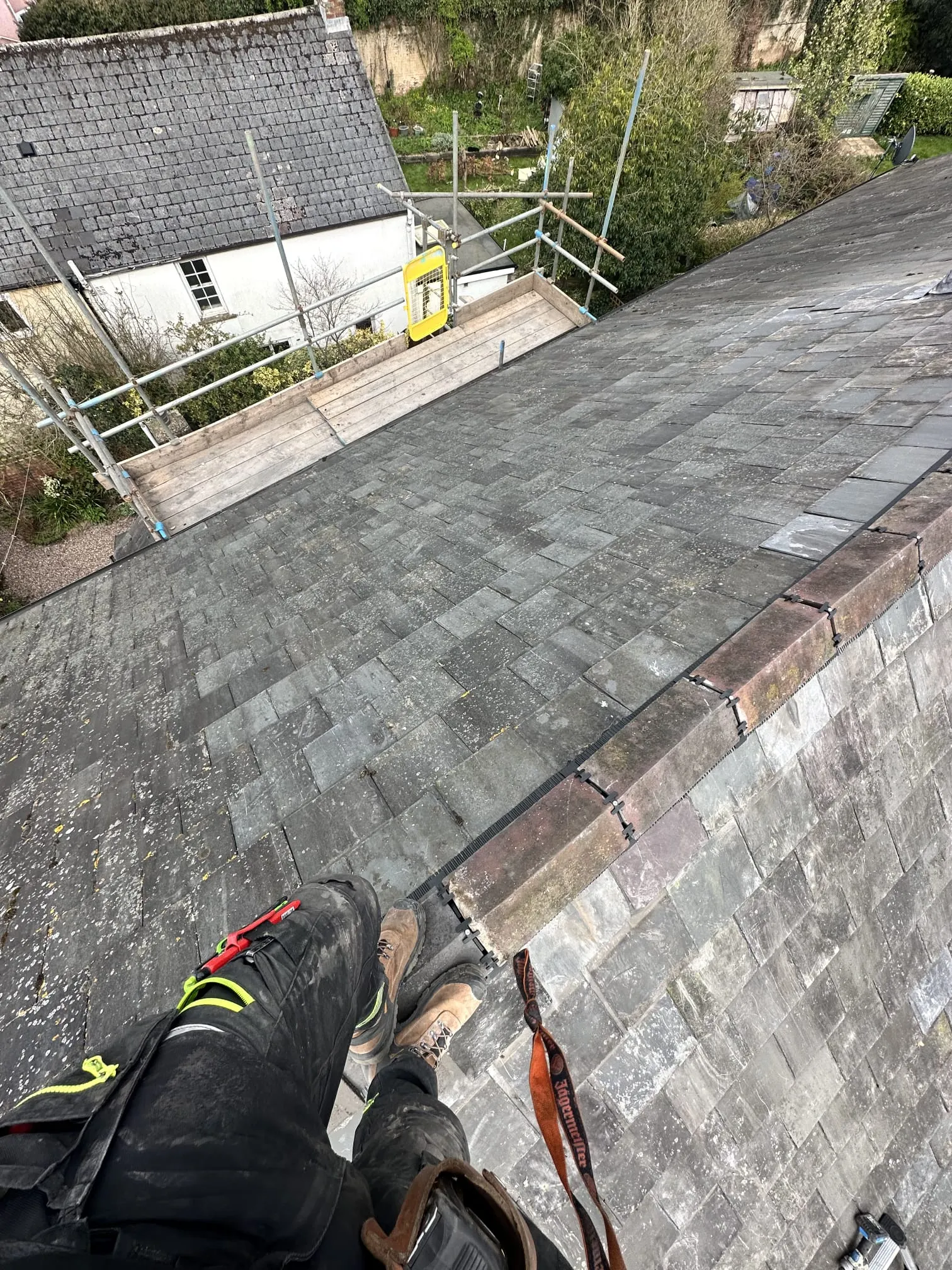 View from above a slate roof, showing individual tiles and scaffolding next to a house.