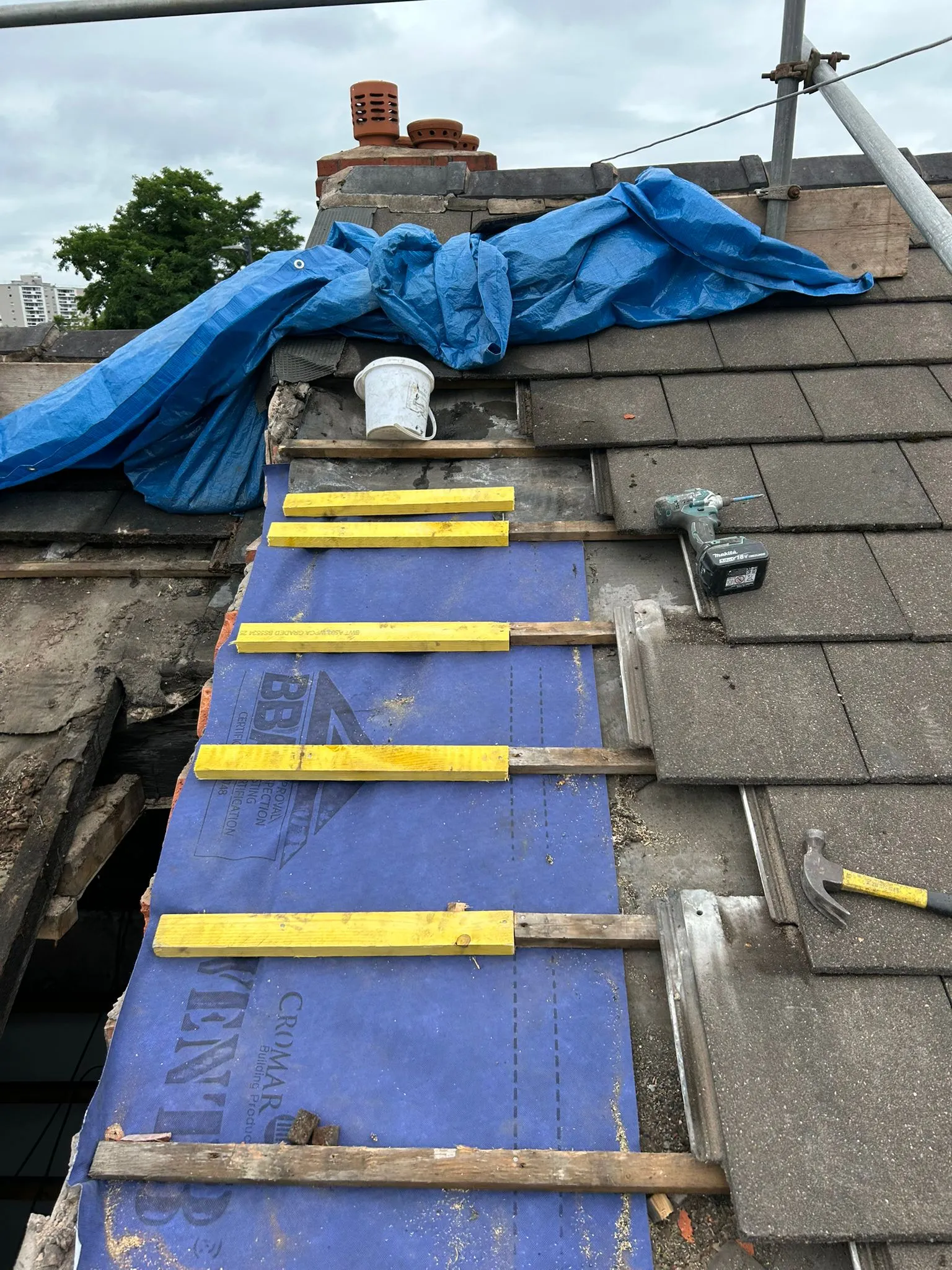 Pitched roof repair in progress, with old tiles removed and new underlayment and battens installed, featuring a blue protective tarp.