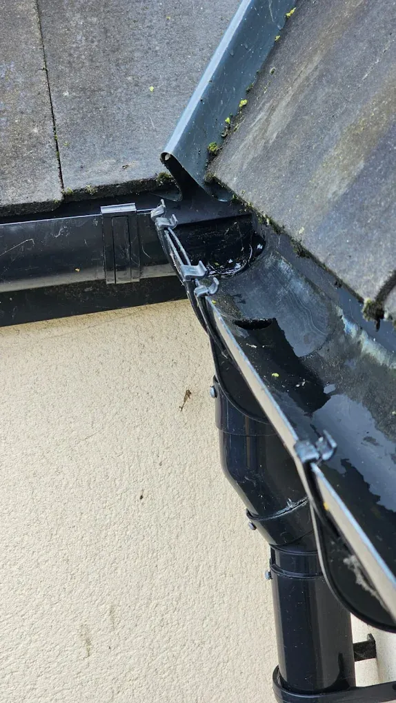 Blocked gutter overflowing with water and debris needing cleaning