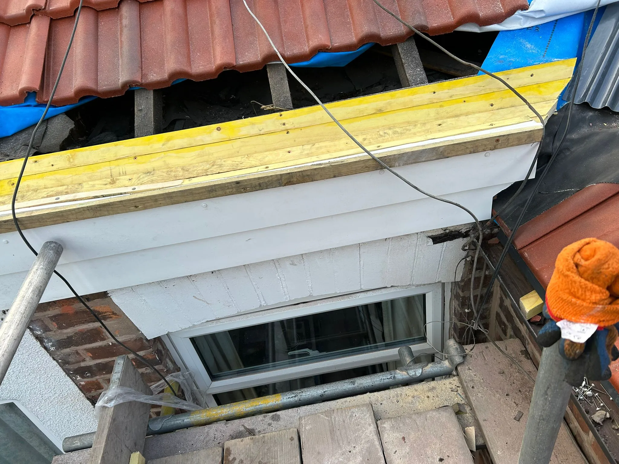 Roof in progress, highlighting a window installation with exposed timber, blue membrane, and roof tiles.