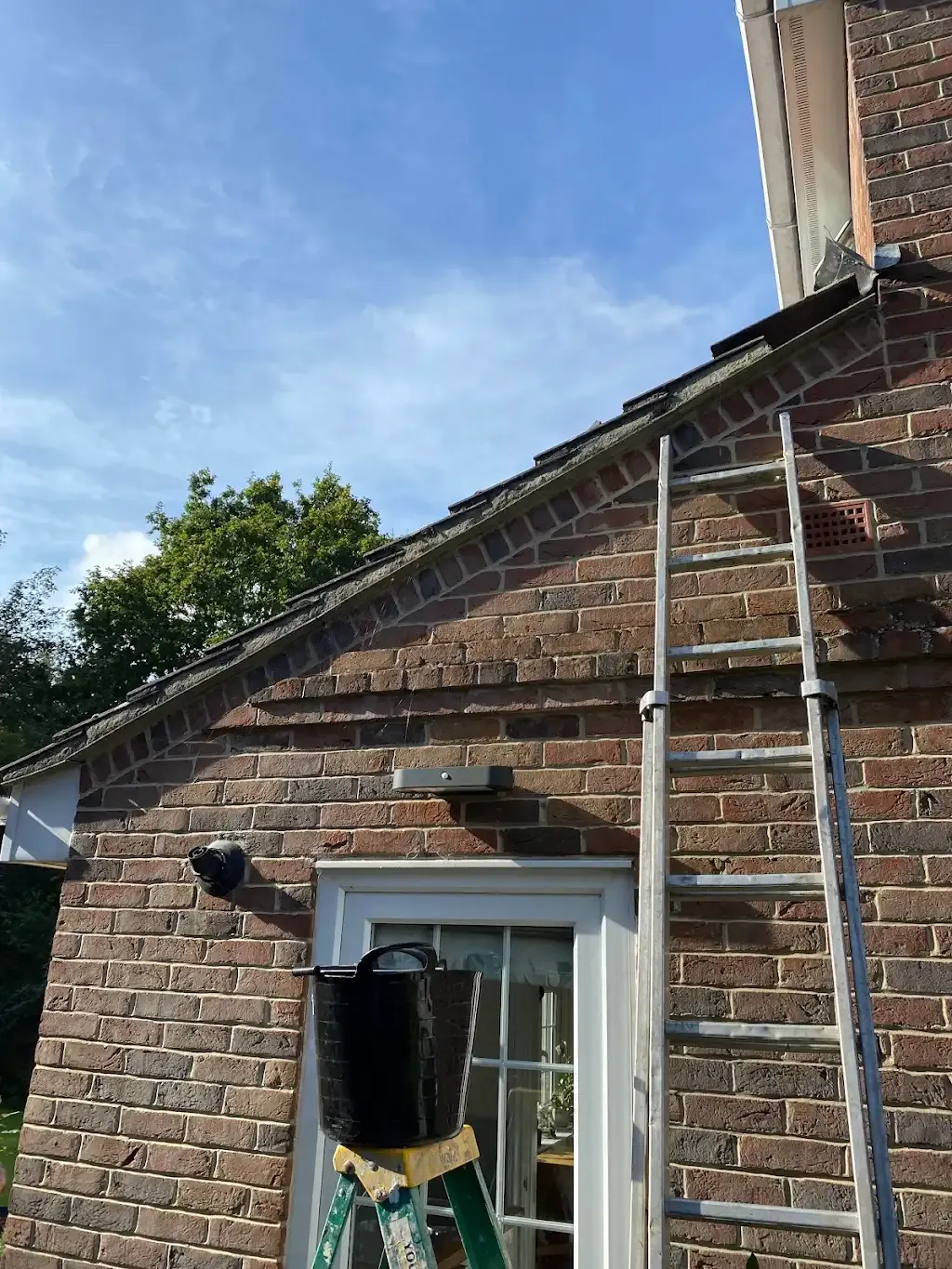 Ladder and bucket ready for roof work on a house wall.
