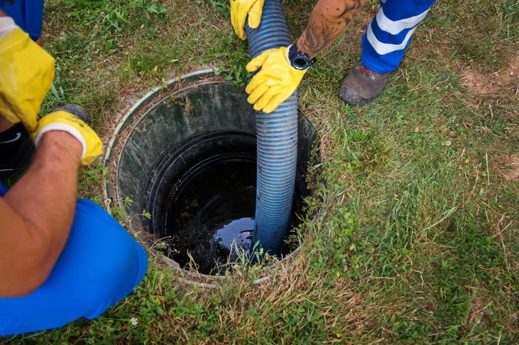 Two drainage technicians using a large hose to work on an open outdoor drain.