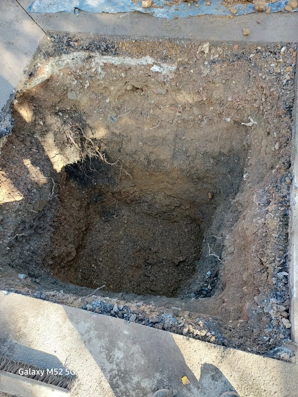 A deep square hole excavated in the ground for drain repair or new drainage system installation.