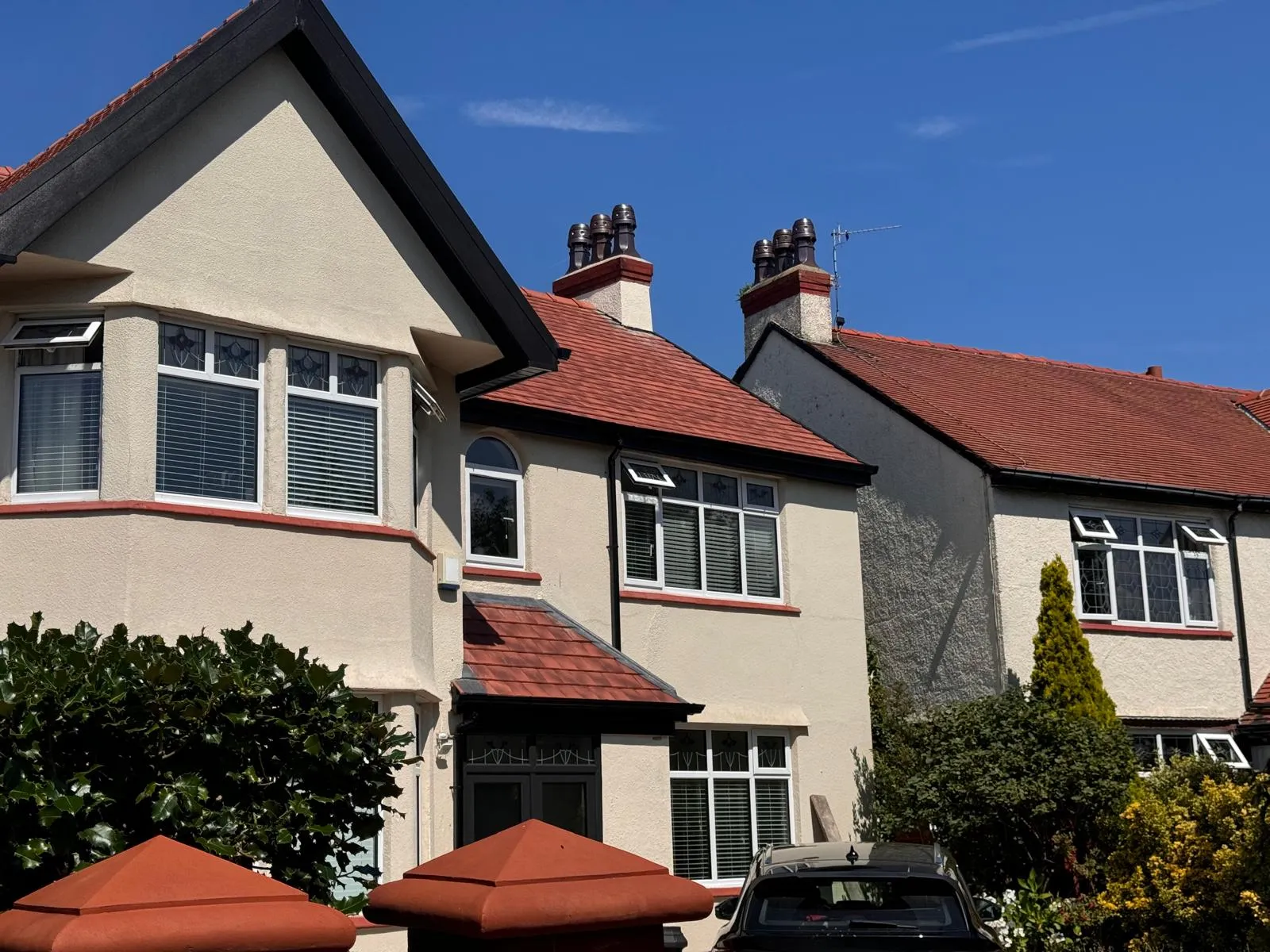 A row of houses with vibrant red tiled roofs and clean cream walls, showcasing quality tiled roofing work.
