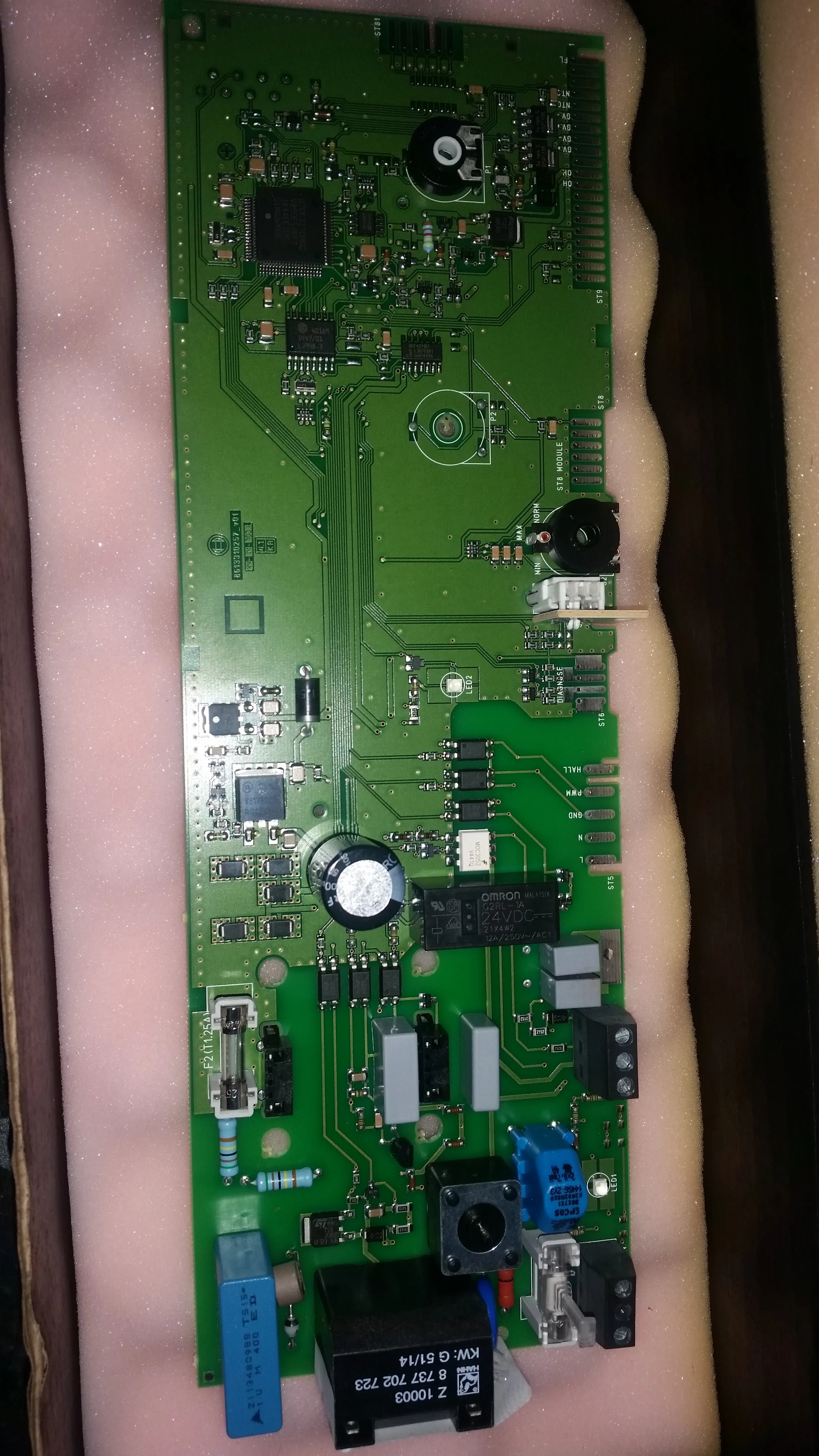 A close-up view of a boiler's main circuit board with chips, capacitors, and connectors.