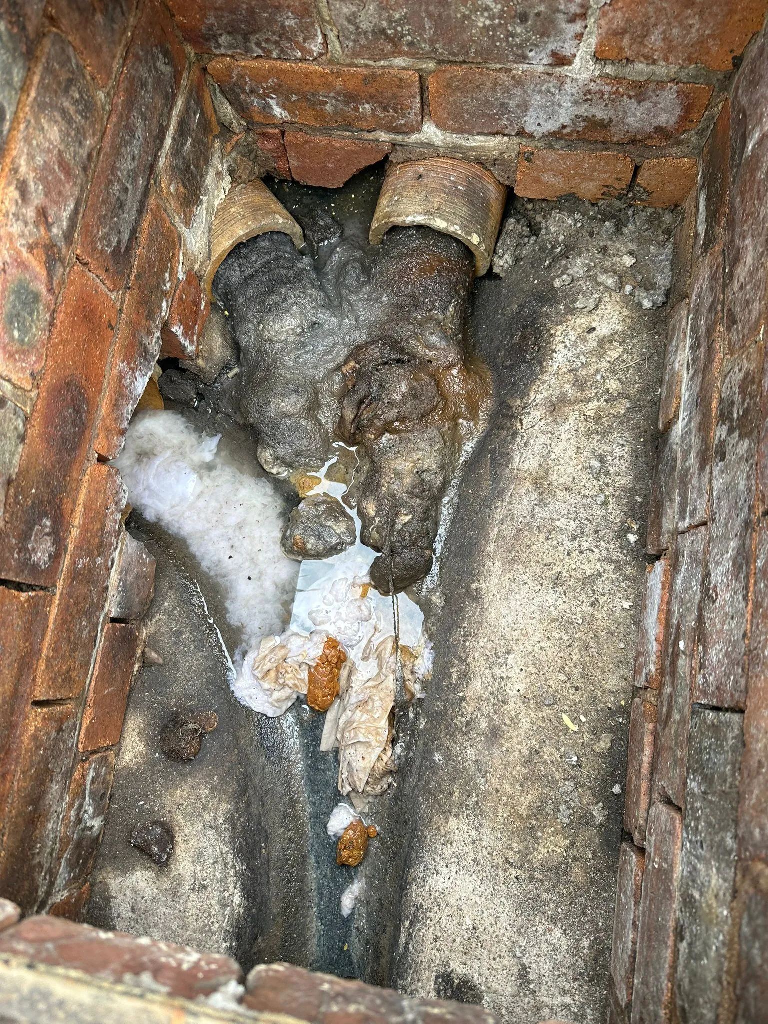 Severely blocked outdoor drain with overflowing sewage and waste inside a manhole.
