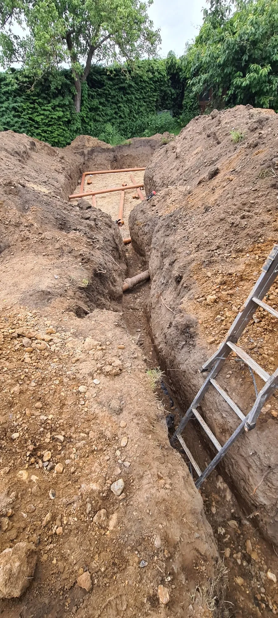 Groundworks excavation for drainage installation with pipes laid in a trench, ready for a new sewage system or soakaway.