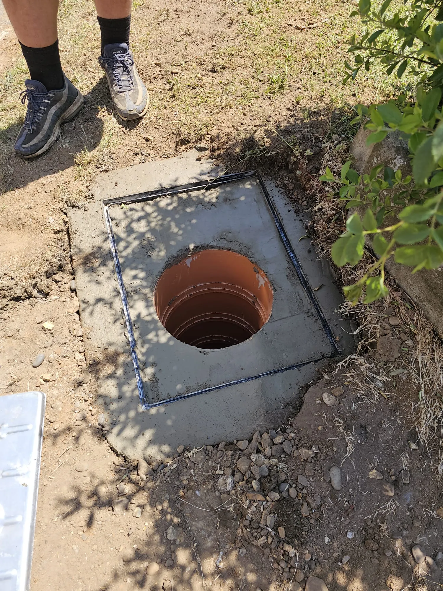 A newly installed drainage inspection chamber with an orange pipe, part of a groundworks or drainage installation project.