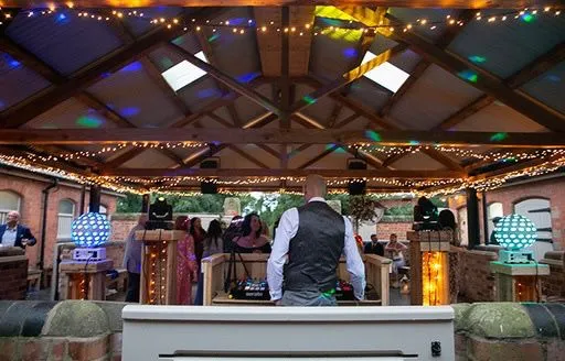 Rear view of a Disco Entertainers DJ at an evening party, surrounded by dazzling disco ball lights, fairy lights, and happy guests on the dancefloor.