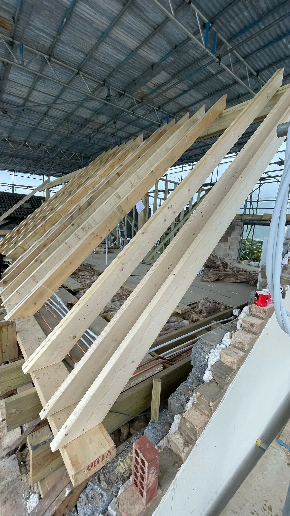 Timber roof rafters being installed on a house construction site under temporary scaffolding cover.