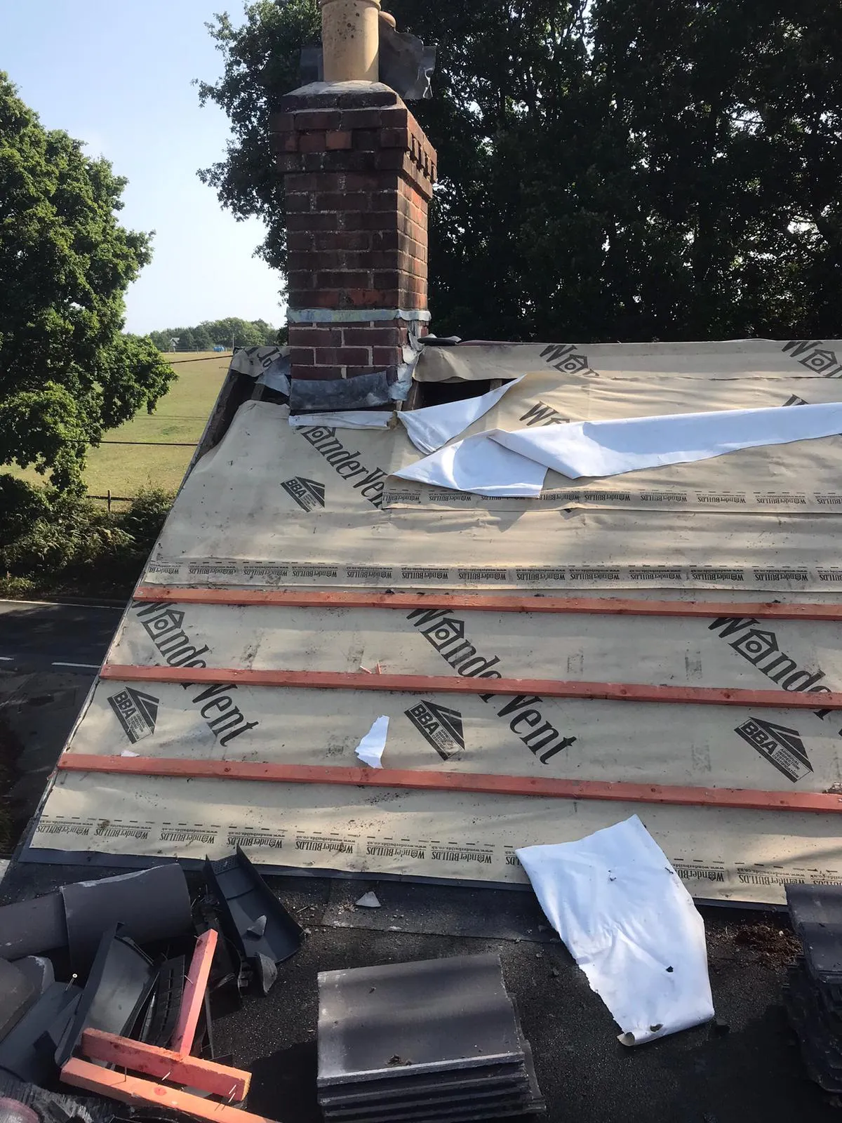 Roof repair in progress with a brick chimney, new roofing underlayment, and timber battens laid out, ready for tile installation.