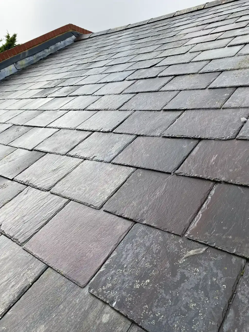Detail of a pitched roof showing grey slate tiles and ridge work.