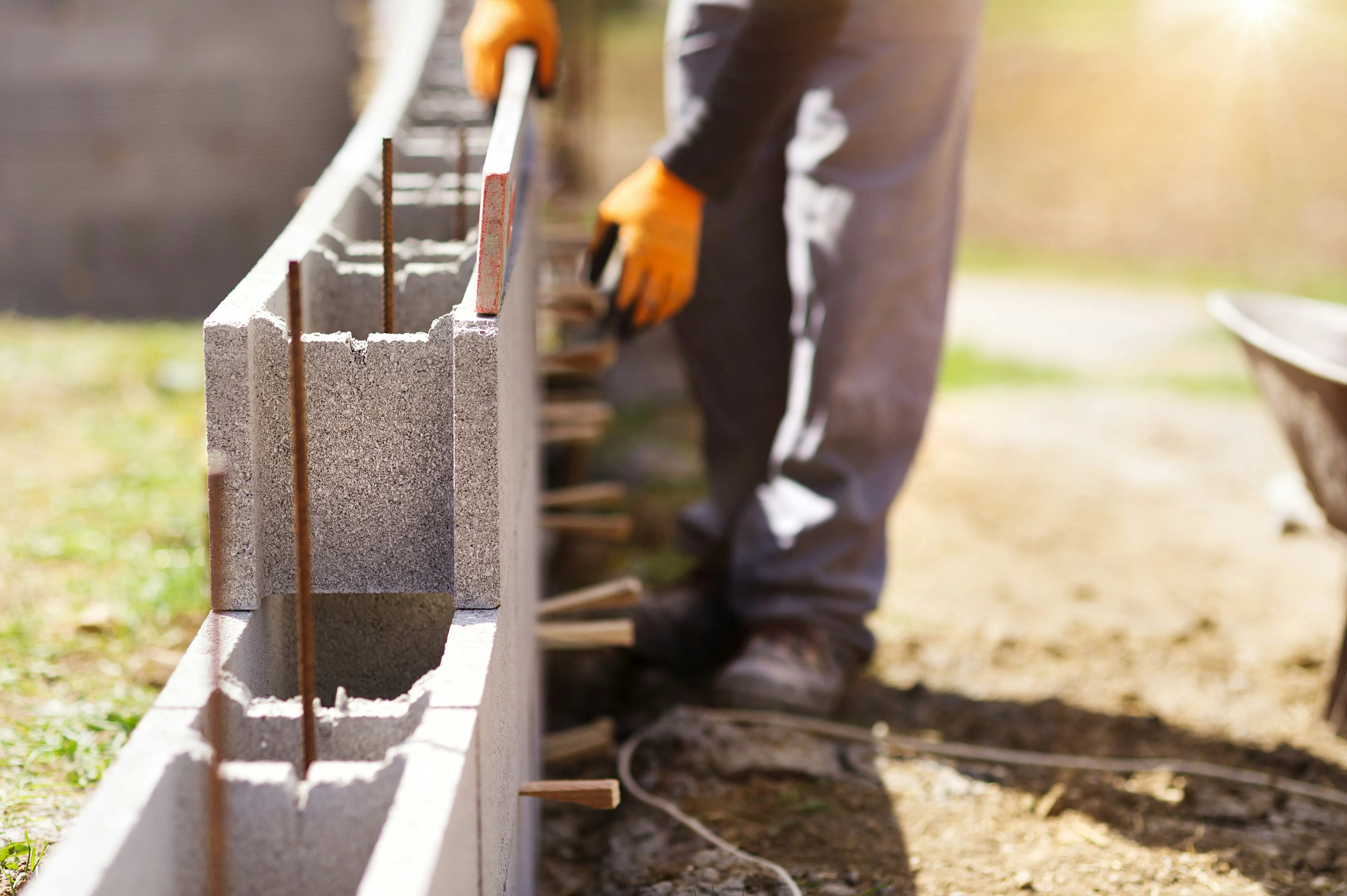 Builder using a level while laying concrete blocks for a new wall during construction.