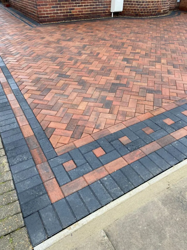 Detailed view of a newly laid block paving driveway in a herringbone pattern with red and brown blocks, bordered by black block paving.